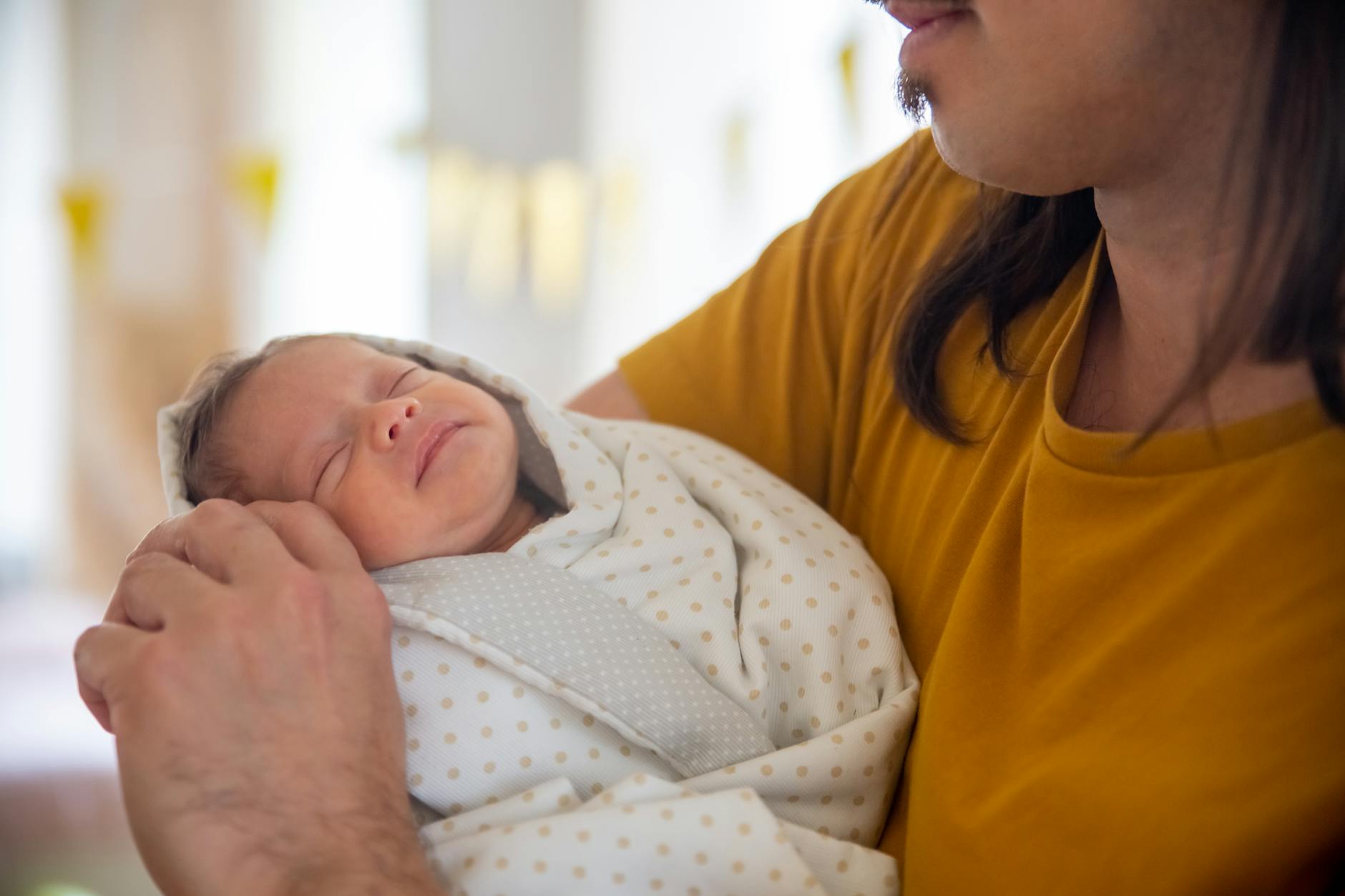 Ilustrasi: A father tenderly holding his sleeping newborn baby indoors, showcasing warmth and bonding.