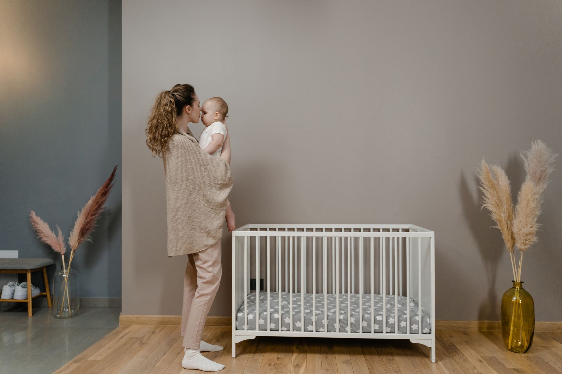 Ilustrasi: A mother gently holds her baby beside a crib in a stylish nursery.
