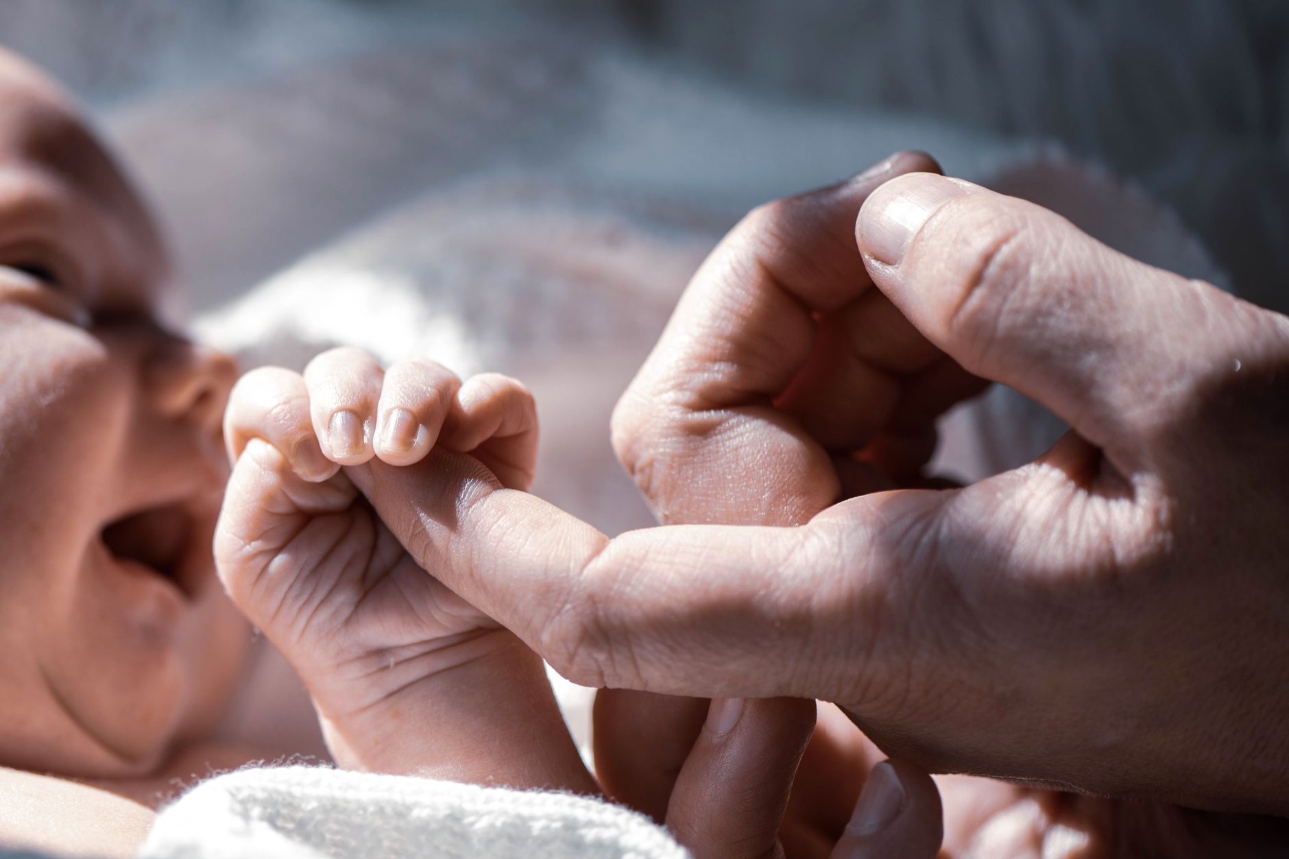 Ilustrasi: Close-up of a newborn baby holding a parent's finger, symbolizing love and connection.