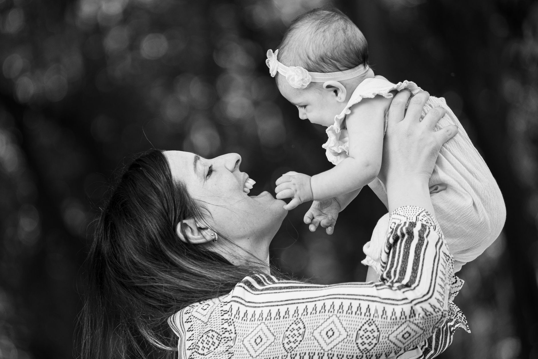 Ilustrasi: A happy mother lovingly holds her baby daughter in an outdoor setting, captured in black and white.