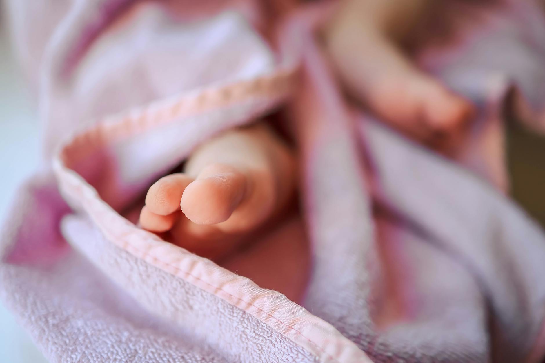 Ilustrasi: Tender close-up of baby feet wrapped in a soft pink blanket, captured with a blurred background.