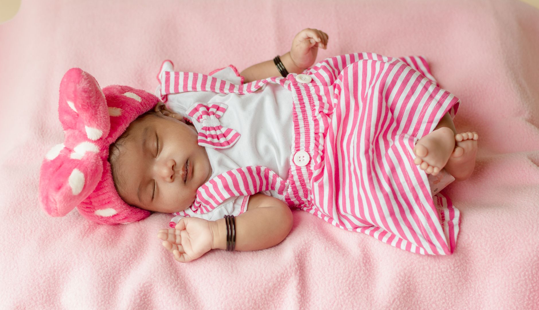 Ilustrasi: A cute newborn baby girl sleeps peacefully in pink striped dress and headband.