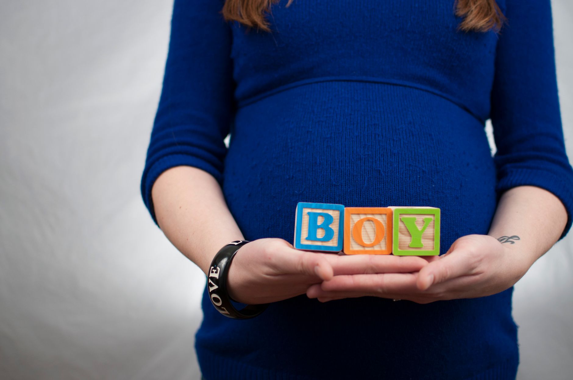 Ilustrasi: Pregnant woman in blue dress holds 'boy' blocks, symbolizing a baby boy announcement.