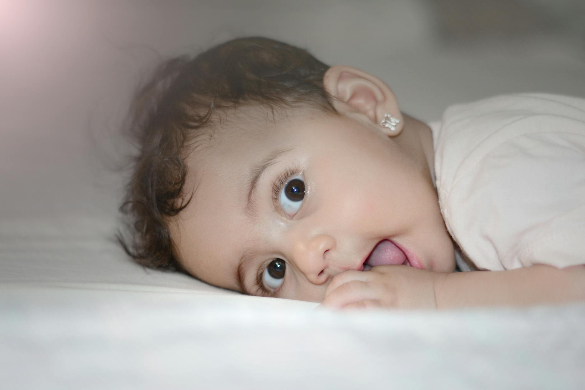 Ilustrasi: Charming baby girl with big brown eyes lying on bed, showing innocence and cuteness.