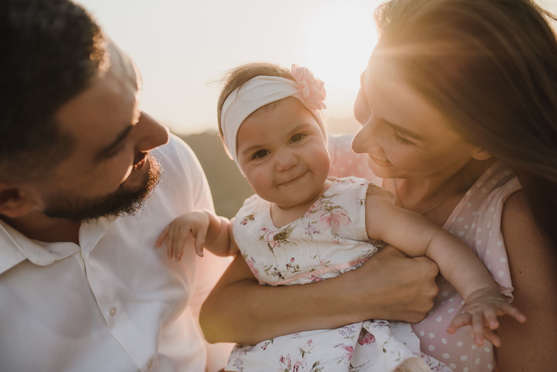 Ilustrasi: A joyful family scene with parents holding their smiling baby at sunset.