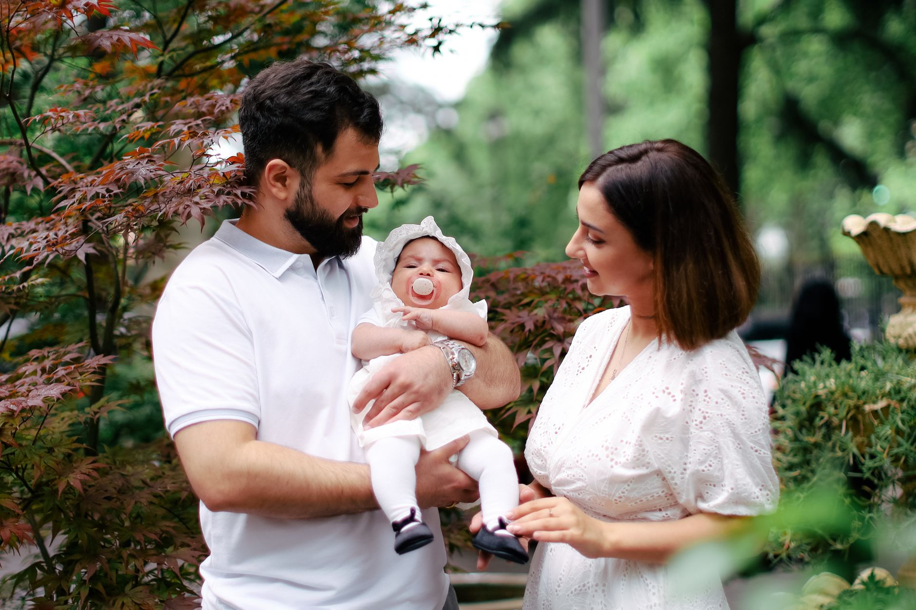 Ilustrasi: A joyful family scene featuring parents holding their newborn baby outdoors, capturing a loving moment.