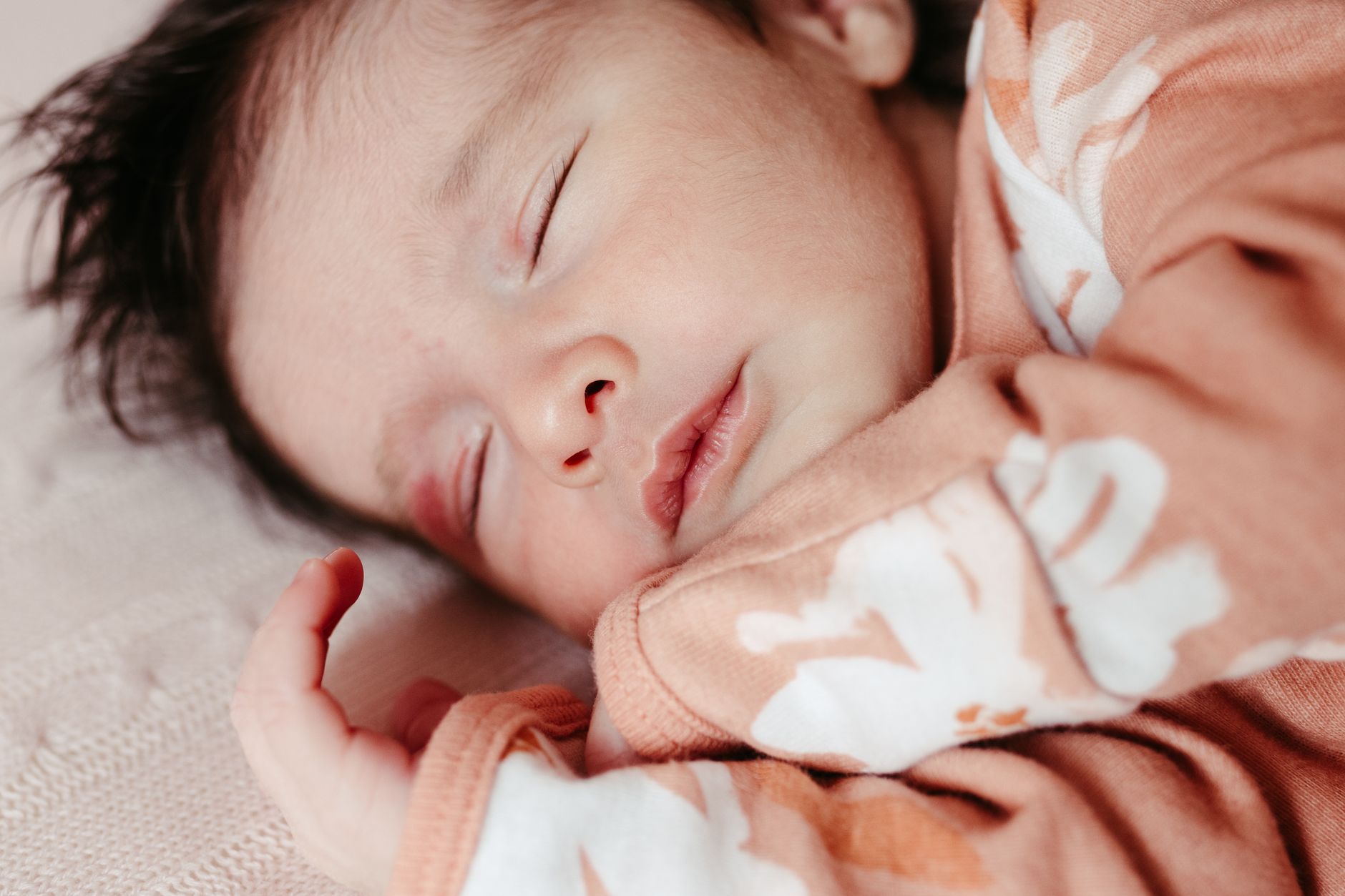 Ilustrasi: Close-up portrait of a newborn baby peacefully sleeping in soft orange clothes indoors.