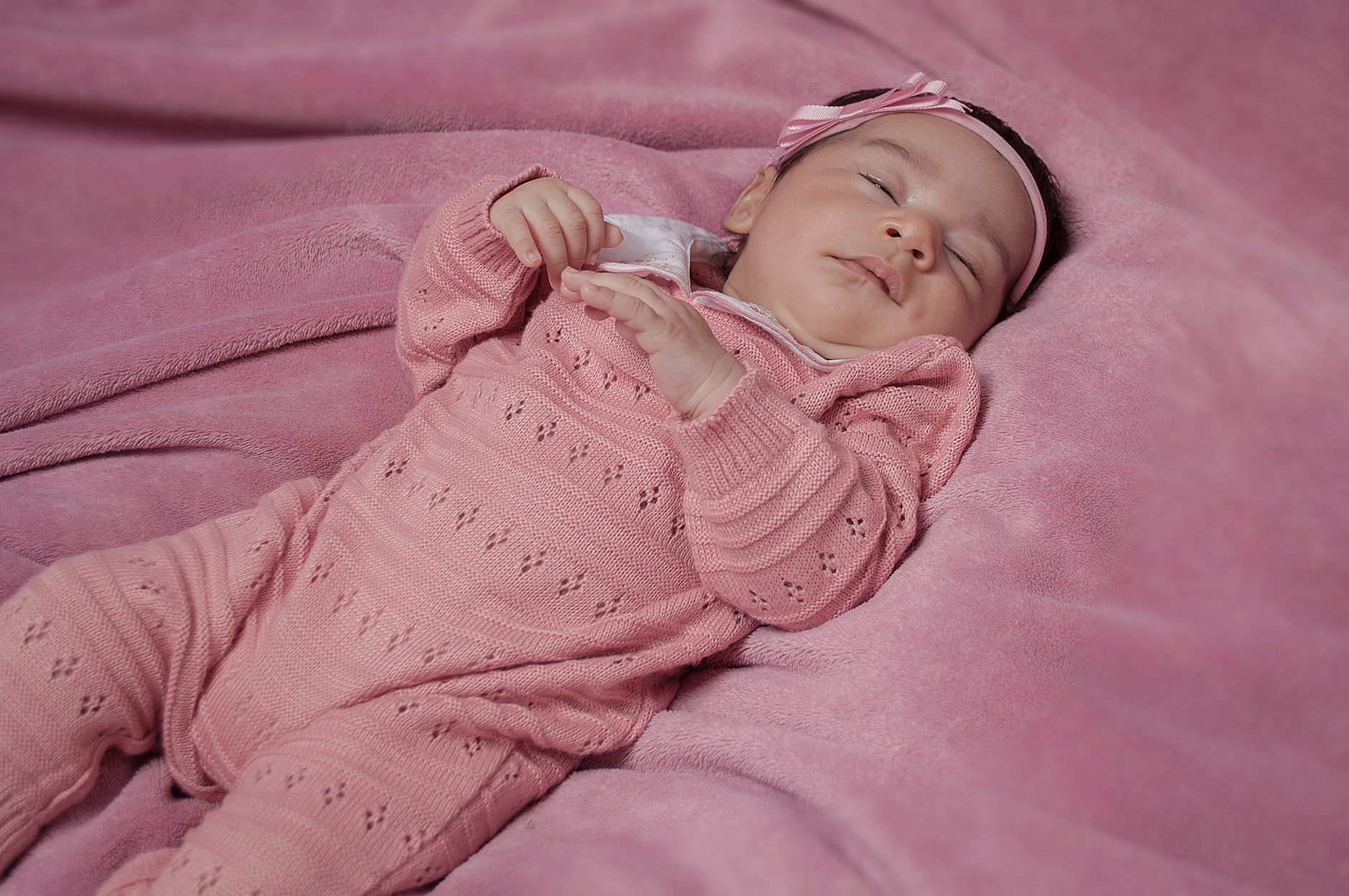 Ilustrasi: A serene baby girl peacefully sleeping on a cozy pink blanket, dressed in pink knitwear.