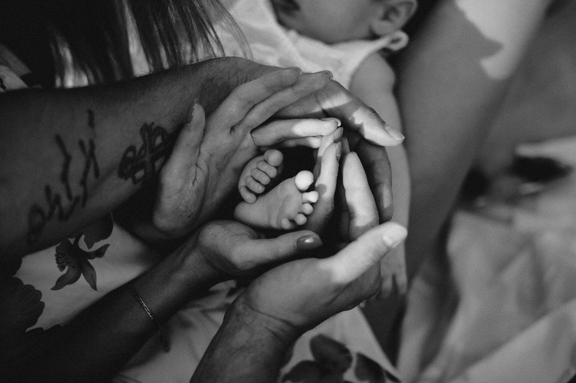 Ilustrasi: Black and white photo of parents lovingly holding their baby's feet, capturing a tender family moment.