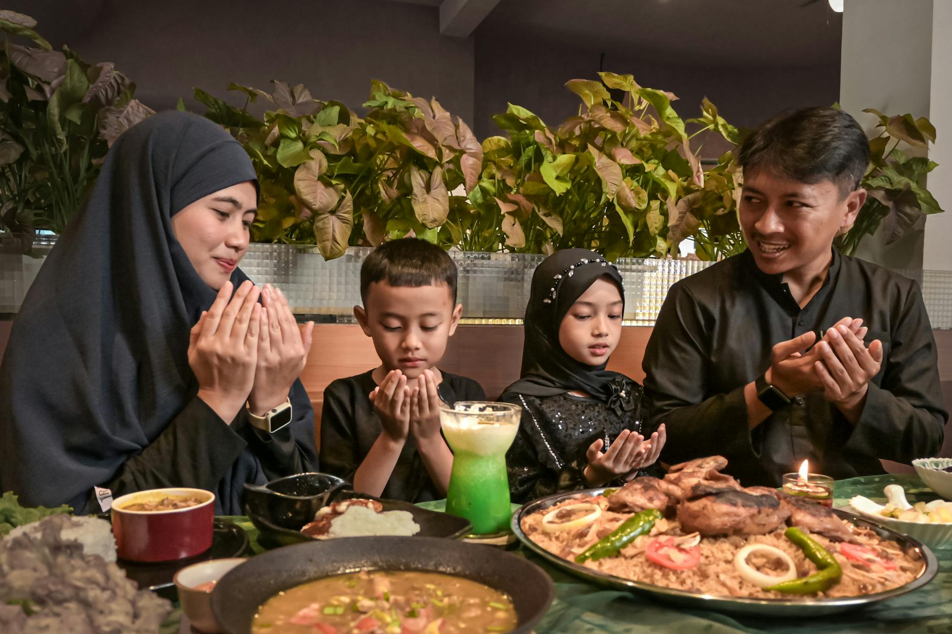 Ilustrasi: Indonesian family in traditional attire prays before enjoying a meal together indoors.