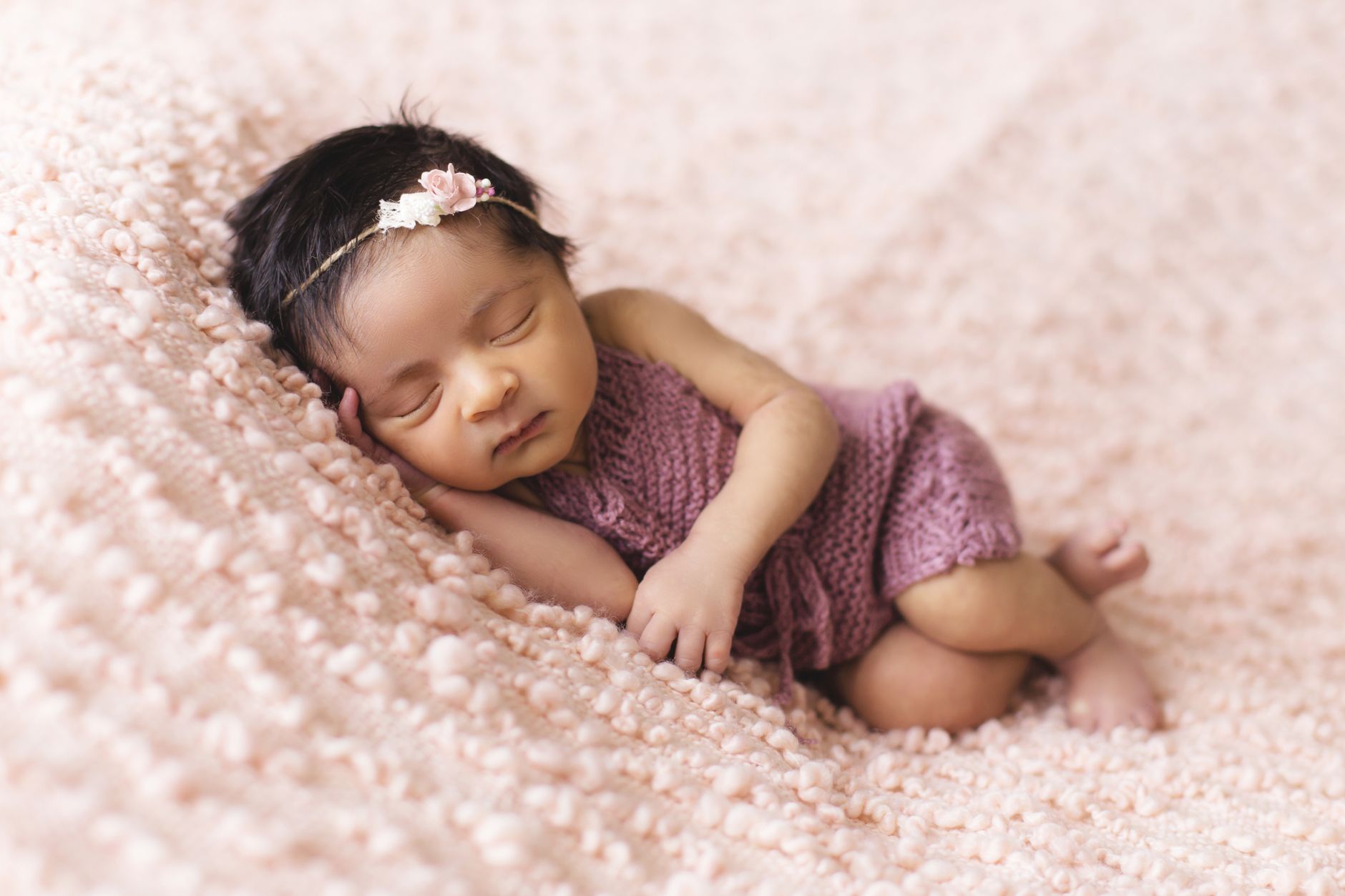 Ilustrasi: A newborn baby girl peacefully sleeps on a soft pink blanket, embodying innocence and tranquility.