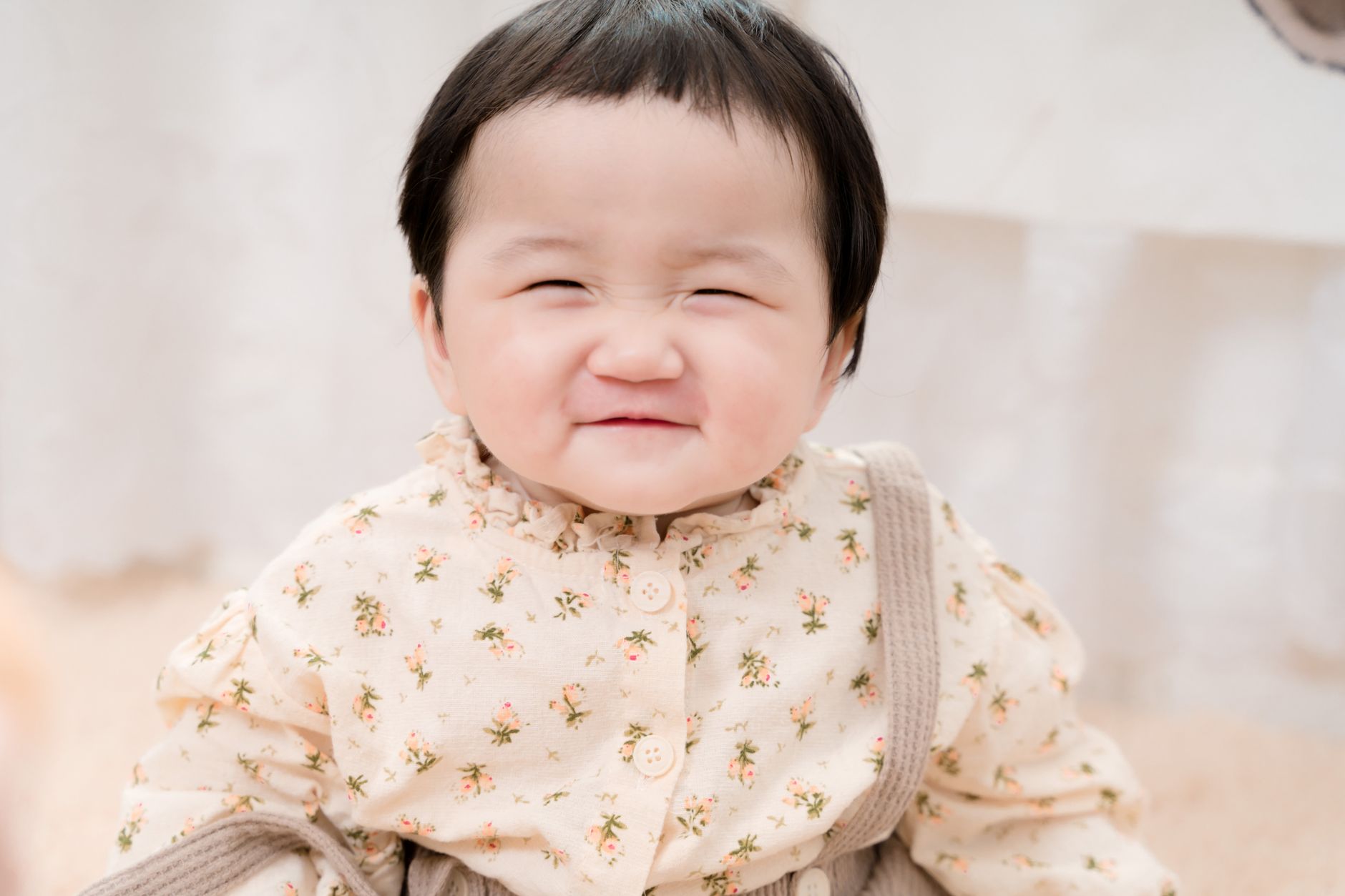 Ilustrasi: A cute baby girl with a floral dress smiling joyfully indoors. Bright and heartwarming portrait.