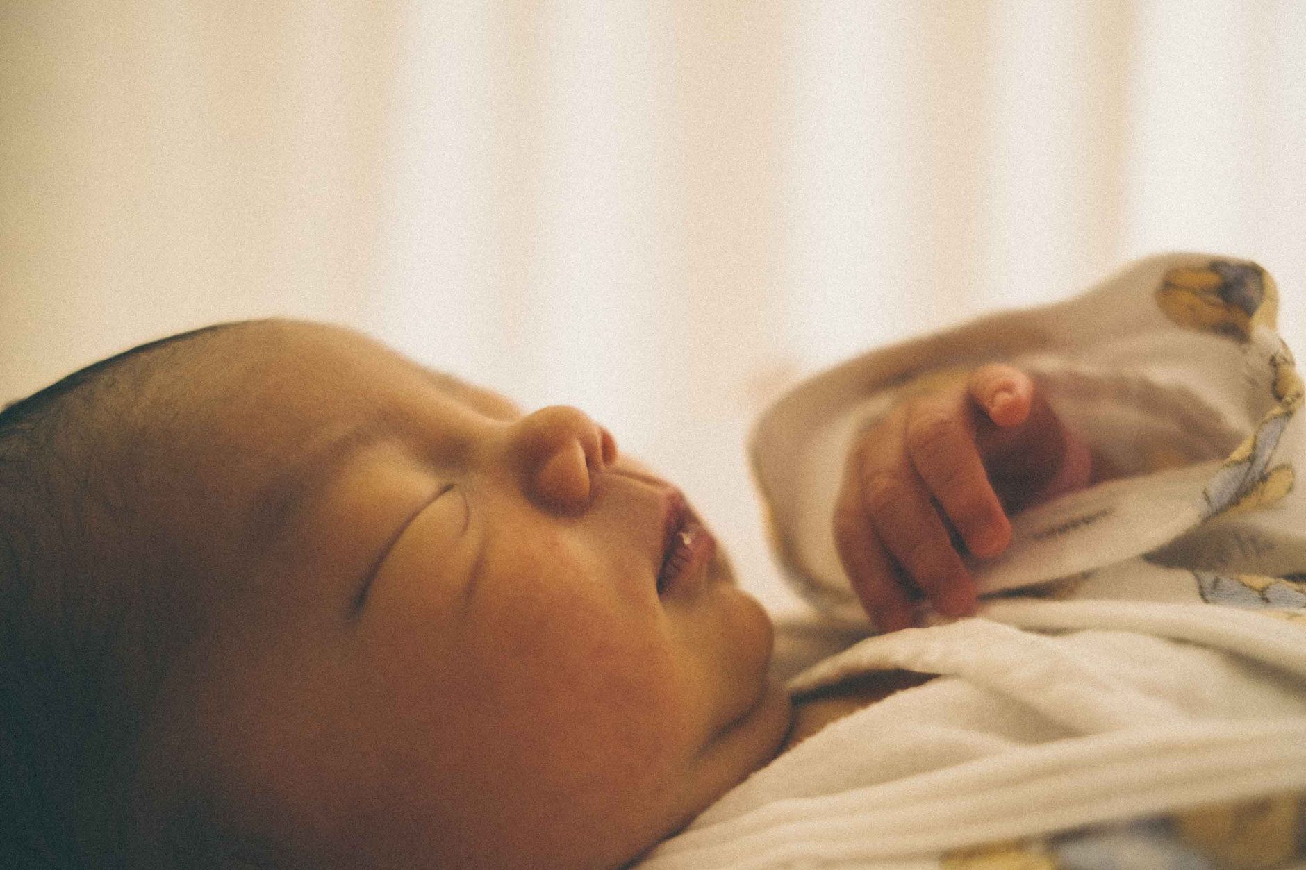 Ilustrasi: Close-up of a serene newborn baby sleeping wrapped in a cozy blanket.