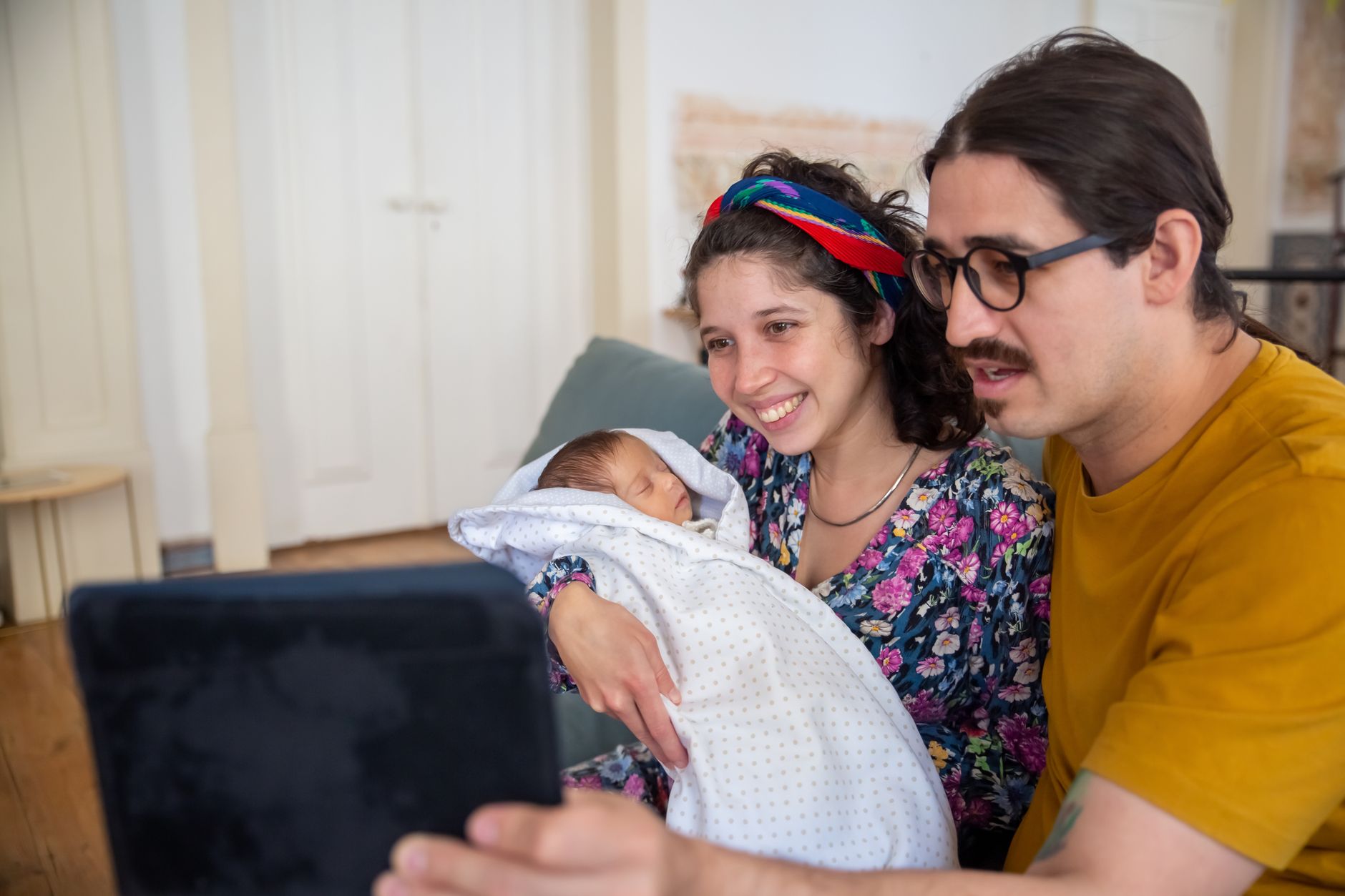 Ilustrasi: A young couple joyfully video chatting with their newborn baby in a cozy home setting.