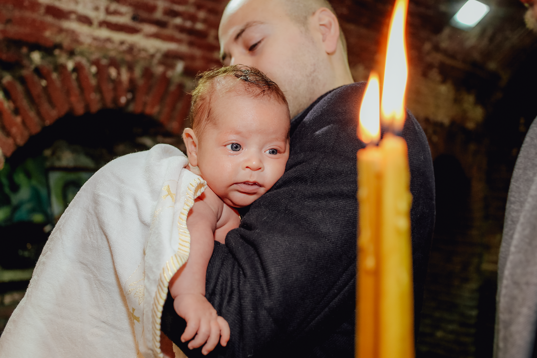 Ilustrasi: Father holding baby during a candle-lit baptism ceremony inside a church.
