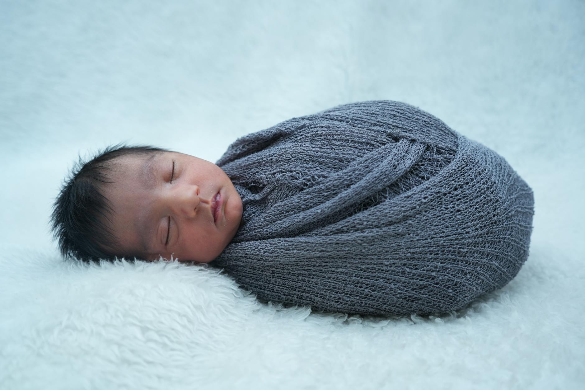 Ilustrasi: A serene newborn baby peacefully sleeping wrapped in a soft gray blanket.