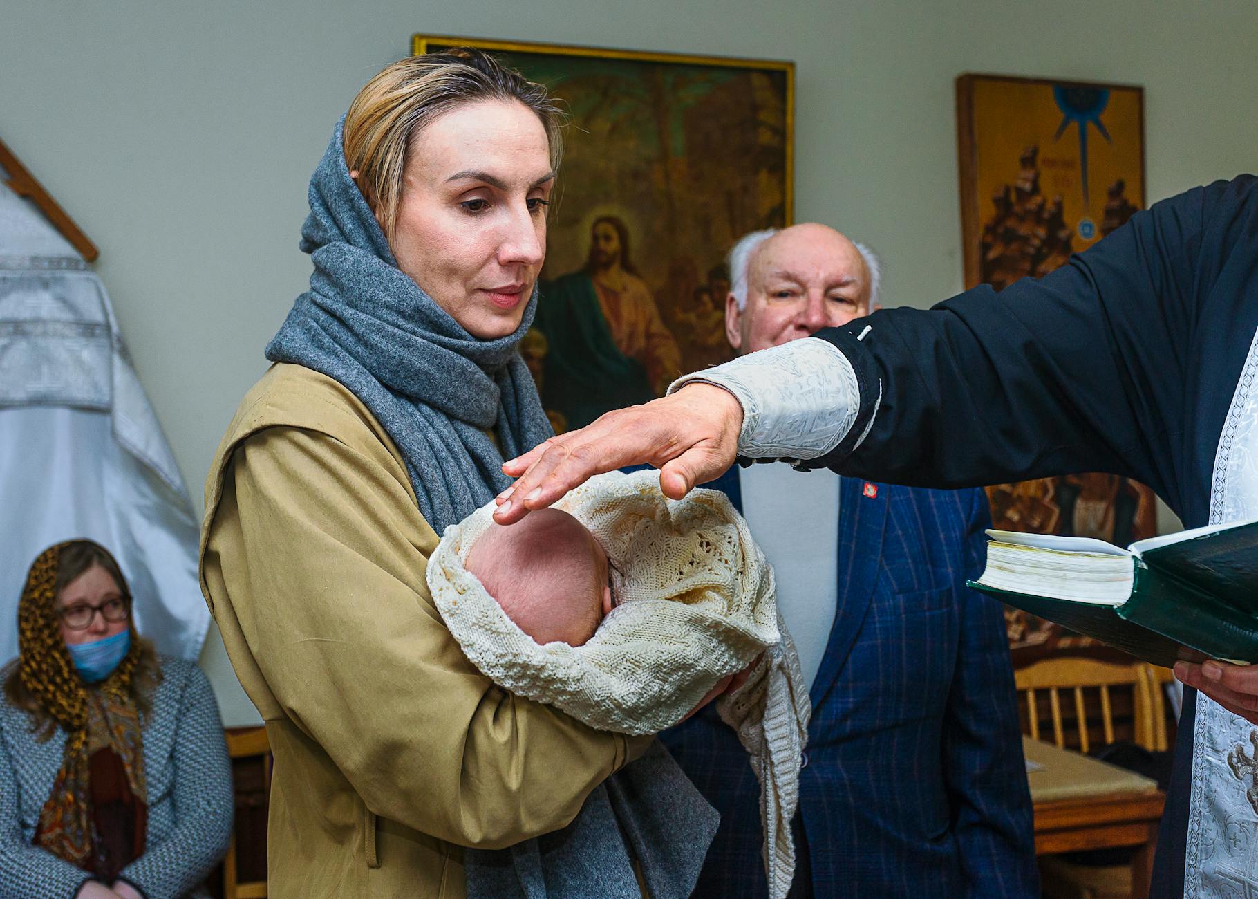 Ilustrasi: A heartfelt baptism ceremony indoors with family members, priest's hand blessing the baby.