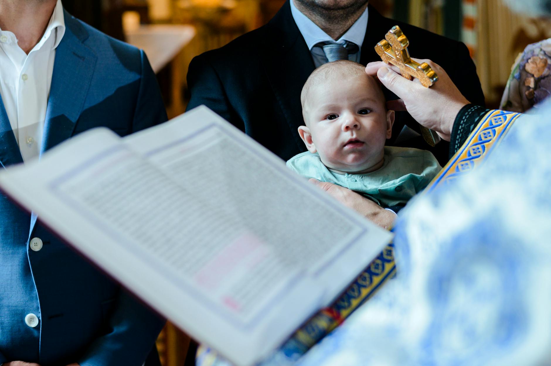 Ilustrasi: A Romanian baptism ceremony showing a priest blessing a baby with holy cross.