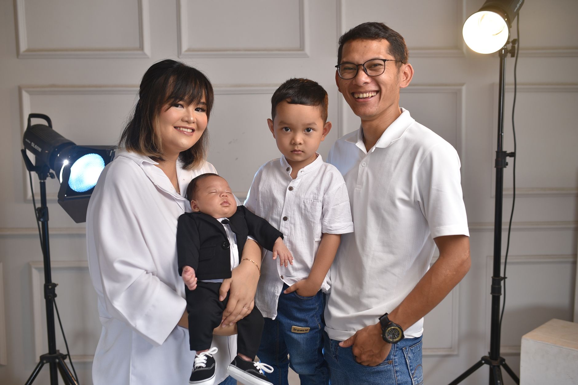 Ilustrasi: A joyful family portrait featuring parents with their newborn and older child in a studio setting.