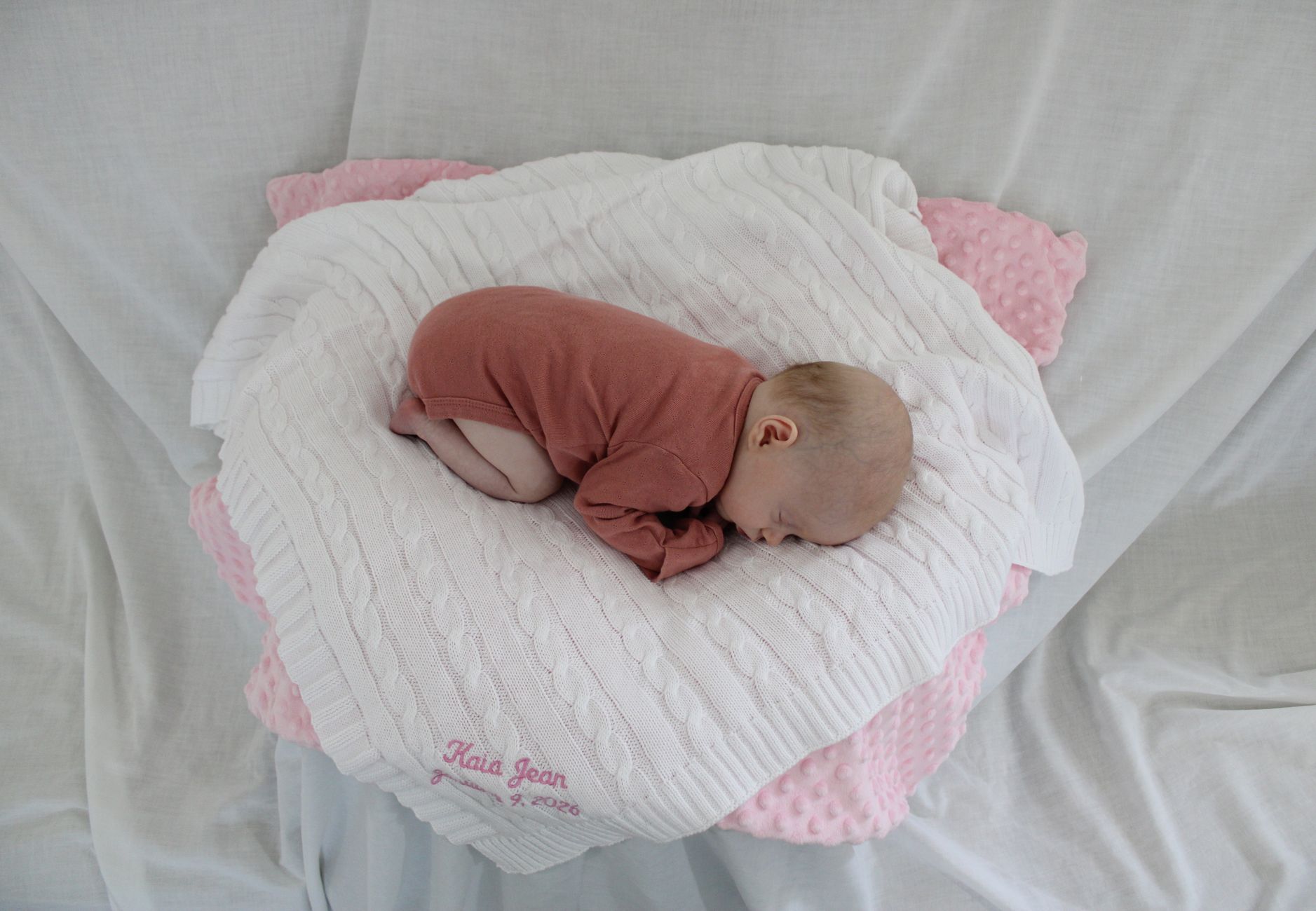Ilustrasi: Newborn baby girl sleeping on pink and white blankets, creating a serene and cute scene.