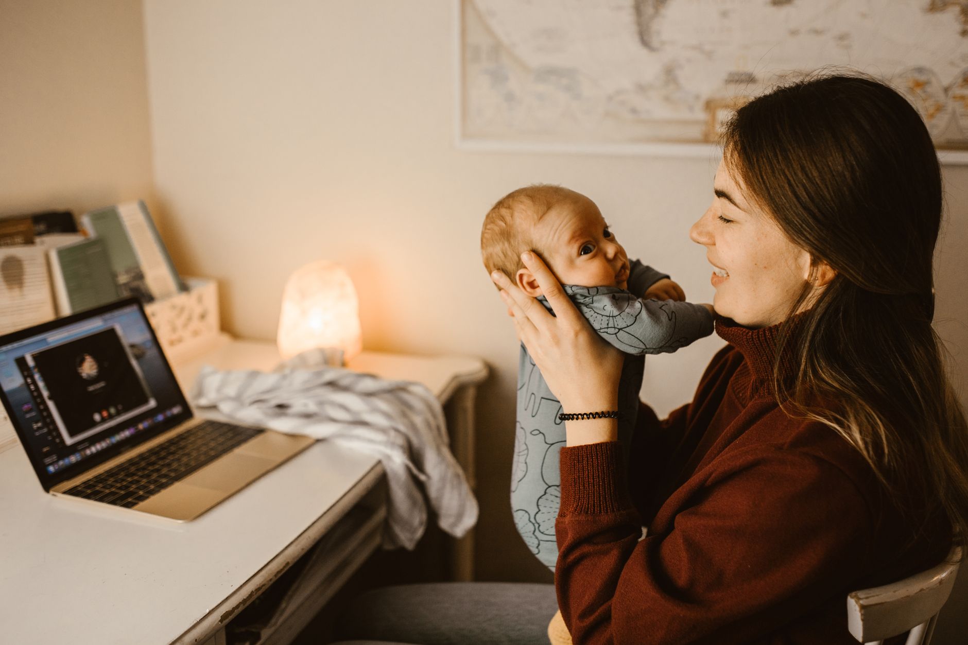 Ilustrasi: Mother holding baby while video calling from home office. Cozy and heartwarming indoor scene.