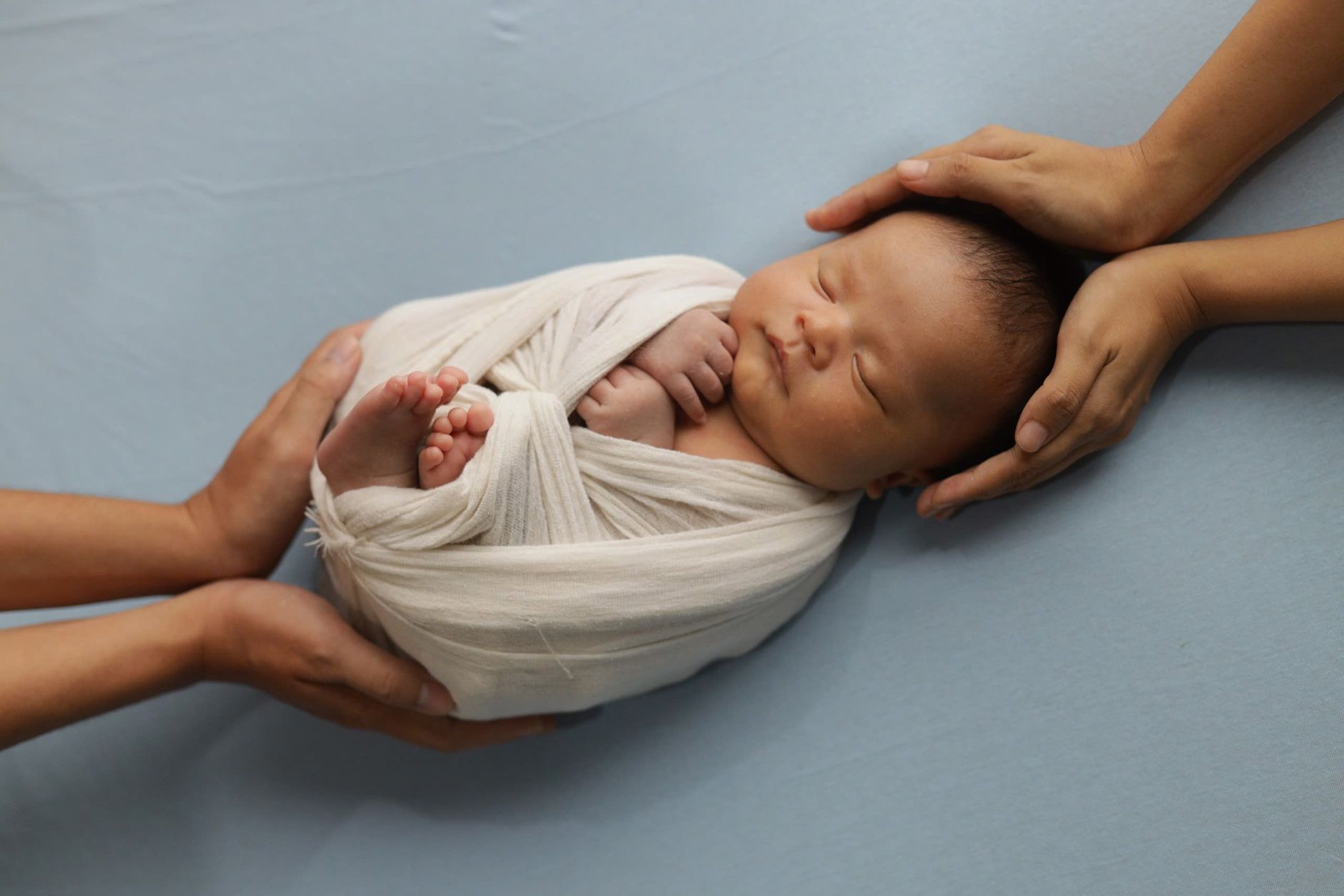Ilustrasi: A peaceful newborn baby wrapped in a soft blanket, surrounded by caring hands.