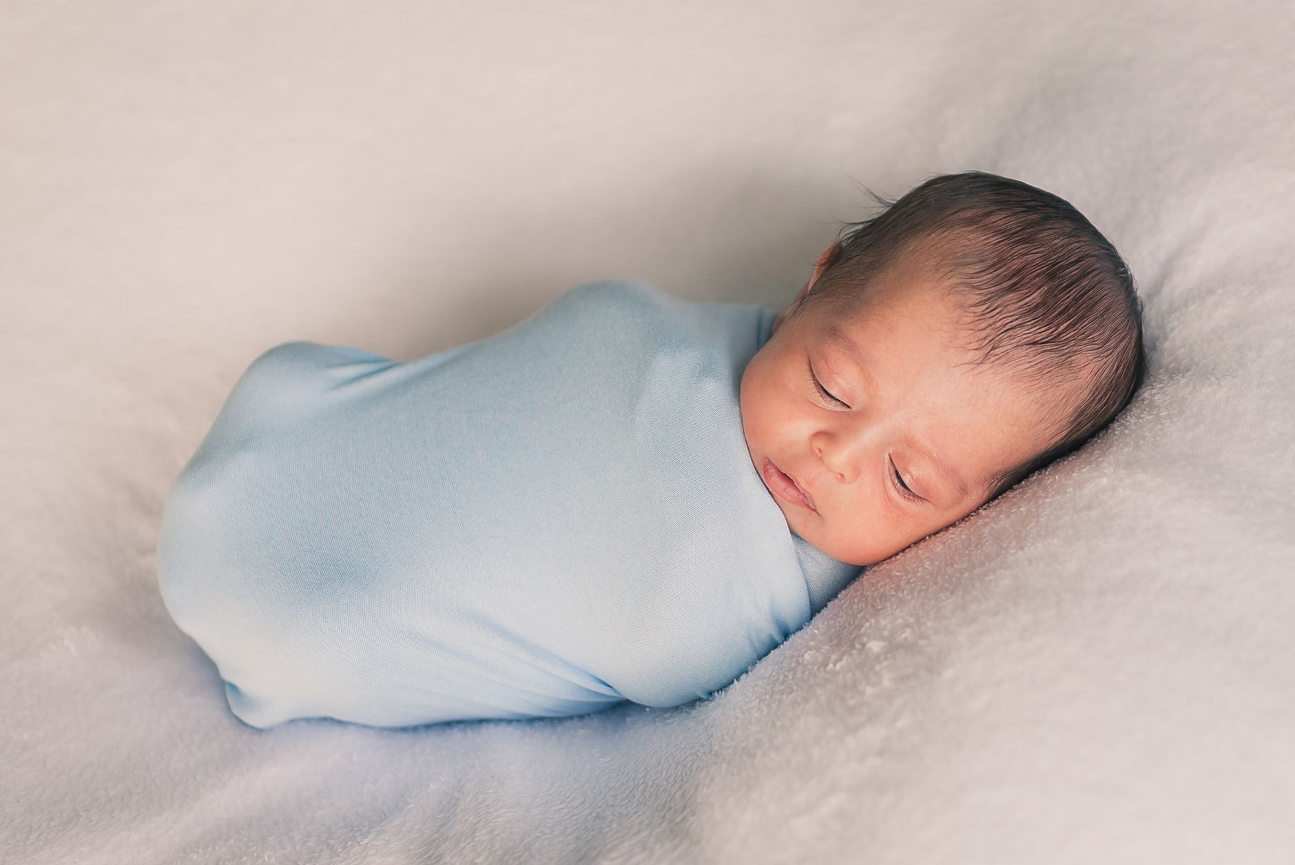 Ilustrasi: A serene newborn baby swaddled in blue, peacefully sleeping on a soft white blanket.