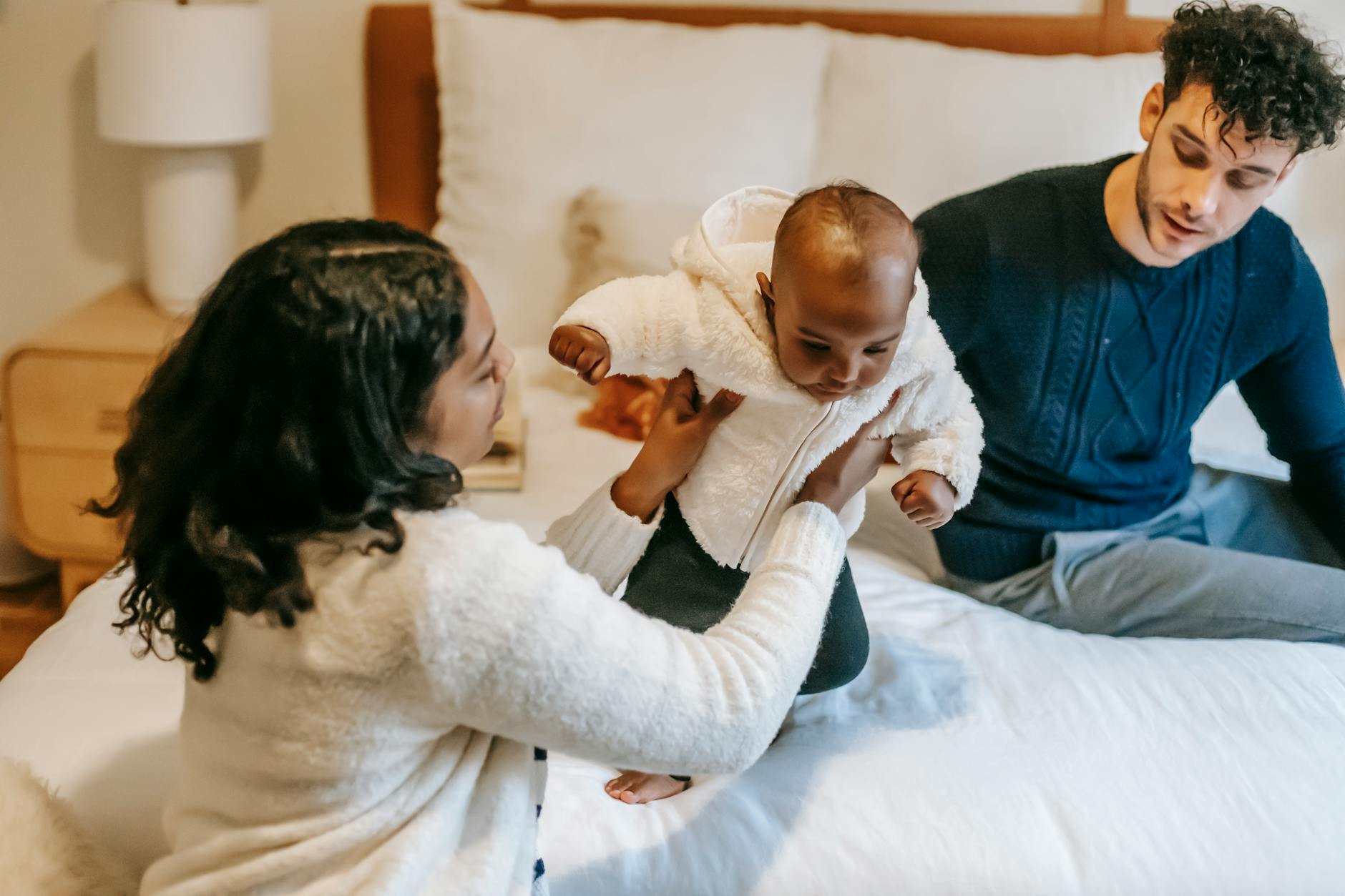 Ilustrasi: High angle of caring African American mom holding cute baby sitting on bed with father