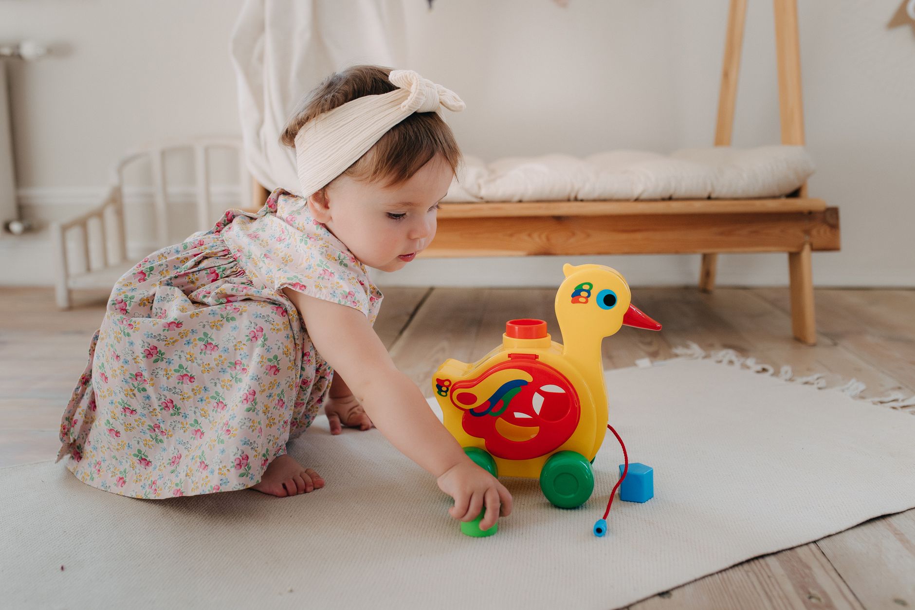 Ilustrasi: Cute baby girl bermain with a colorful duck toy on a white rug in a cozy room.