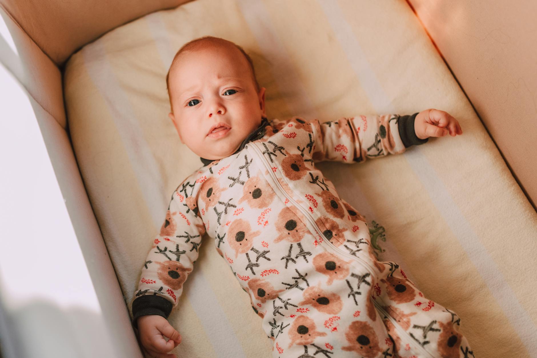 Ilustrasi: Cute baby boy in floral pajamas lying on a cushion in a crib, top view