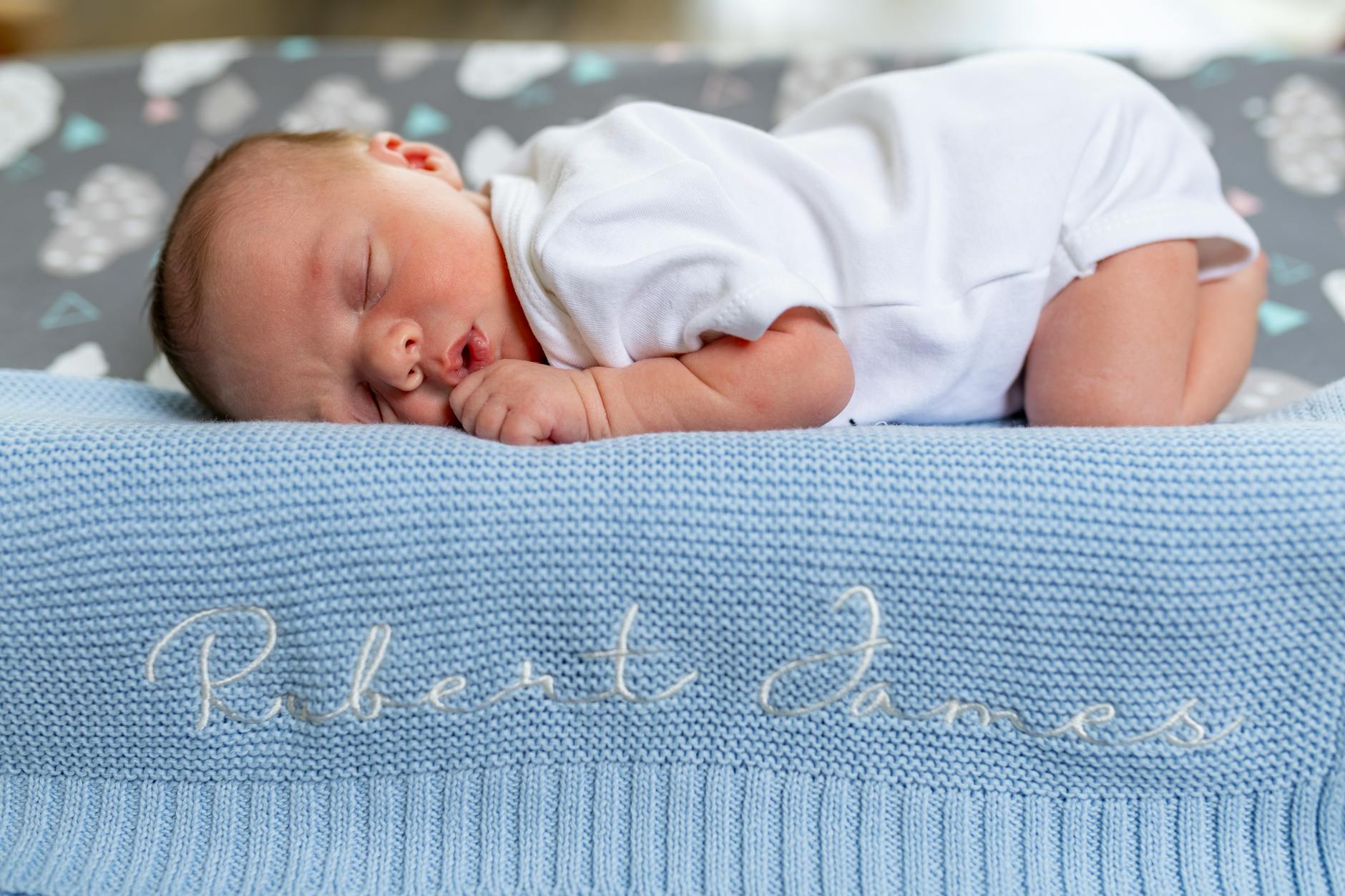 Ilustrasi: A baby sleeps peacefully on a blue knit blanket with name embroidery.