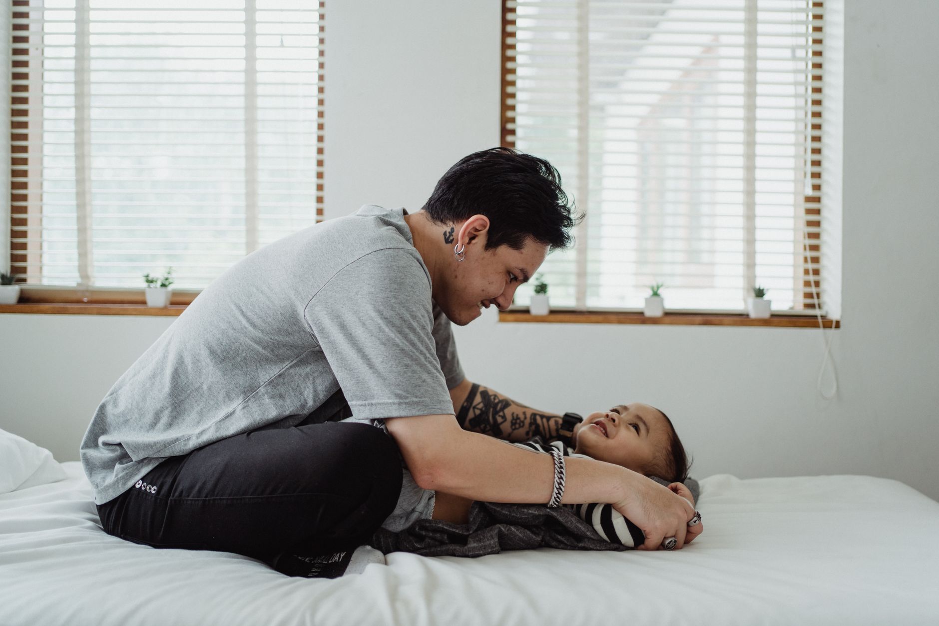 Ilustrasi: A joyful father bermain with his smiling son on a bed in a well-lit room, capturing a tender moment.