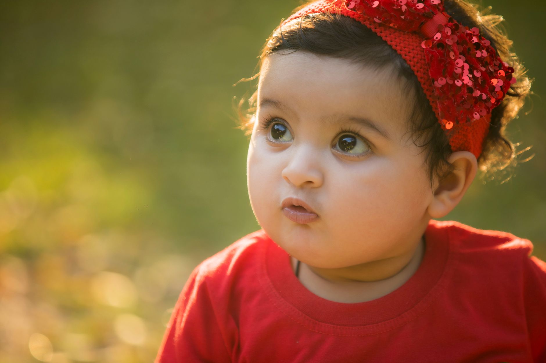 Ilustrasi: Close-up of a cute baby girl in a red headband, enjoying a sunny day outdoors.