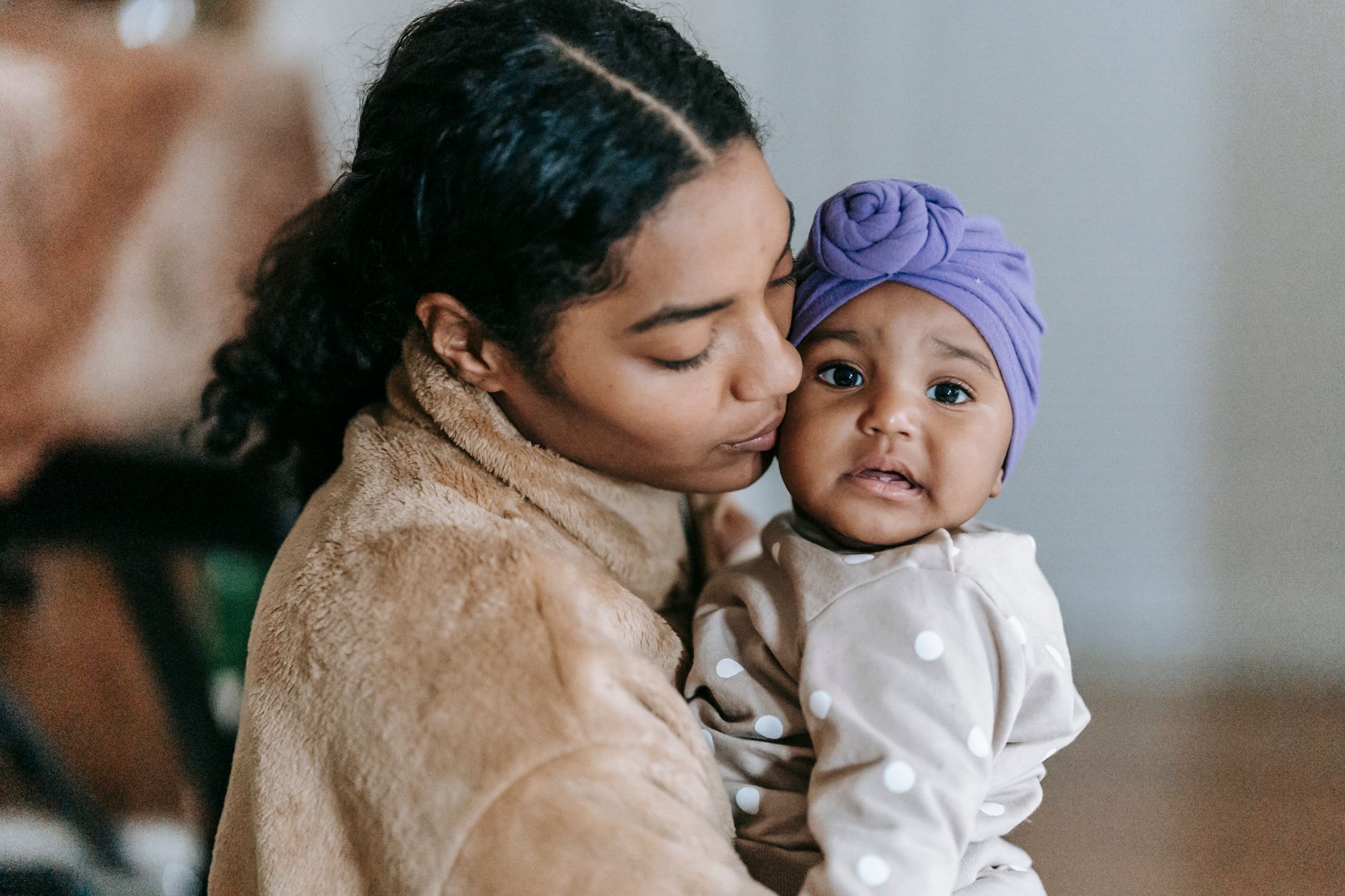 Ilustrasi: Side view of African American mum cuddling baby girl in turban and kissing cheek