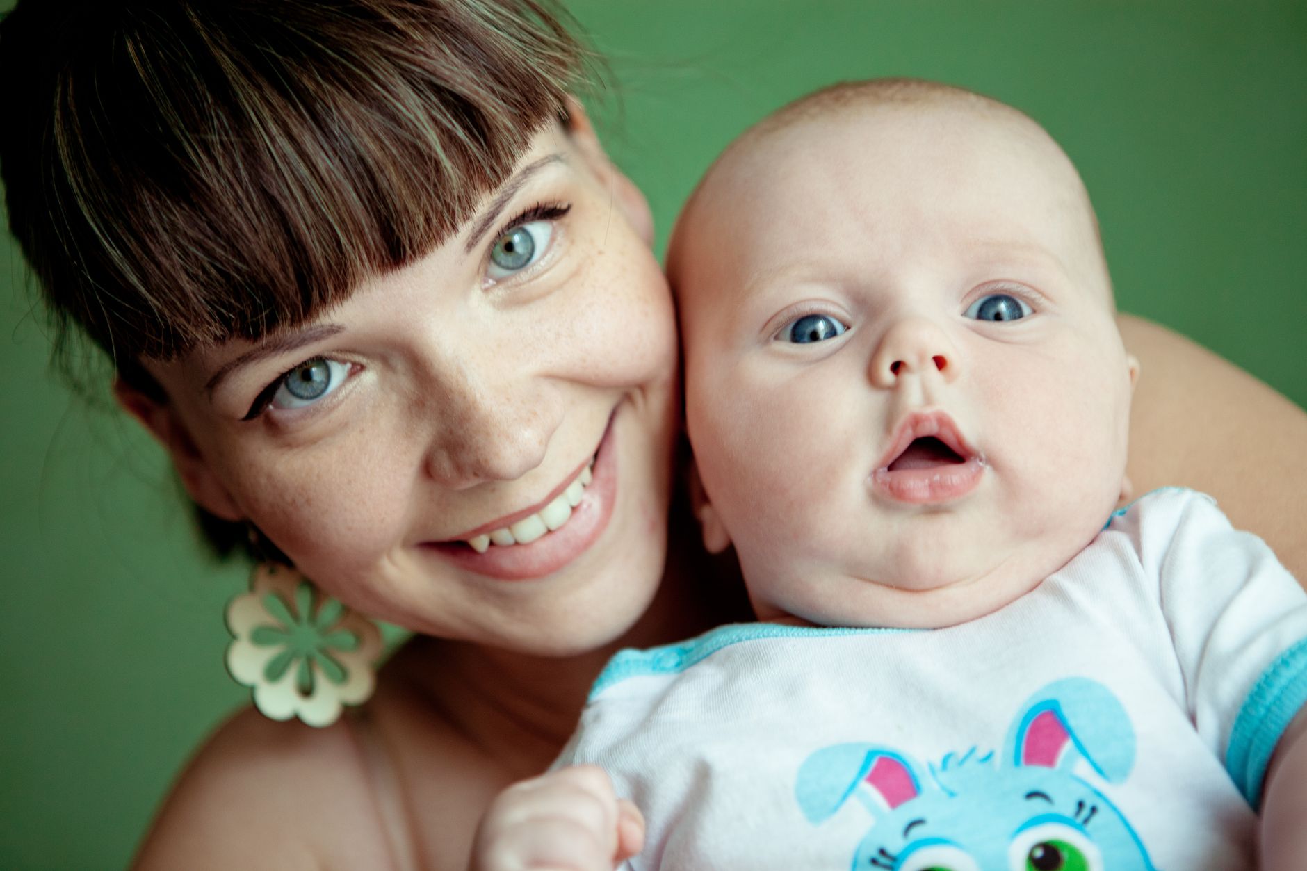 Ilustrasi: Close-up portrait of a smiling mother holding her baby with a joyful expression indoors.