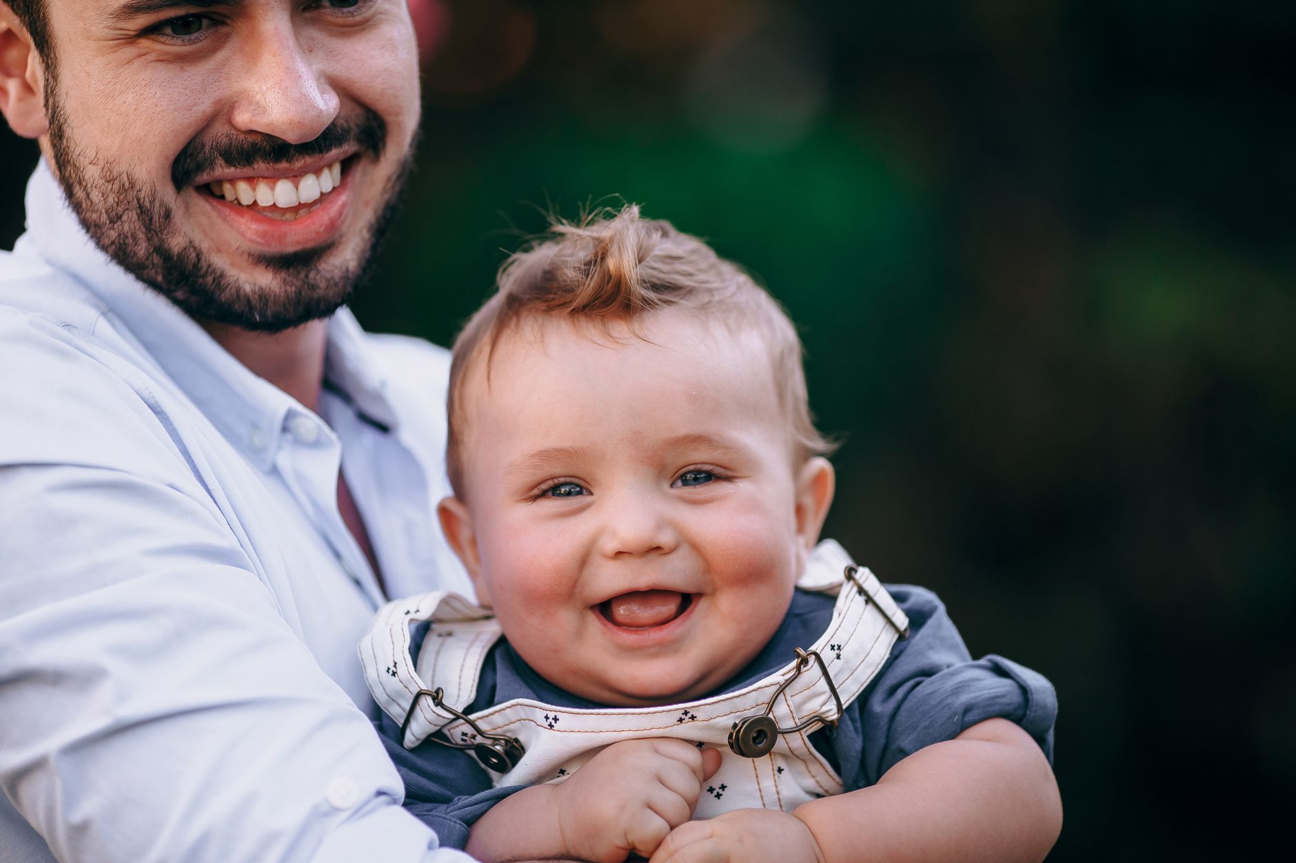 Ilustrasi: A joyful father holding a smiling baby boy outdoors, showcasing happiness and family bonding.