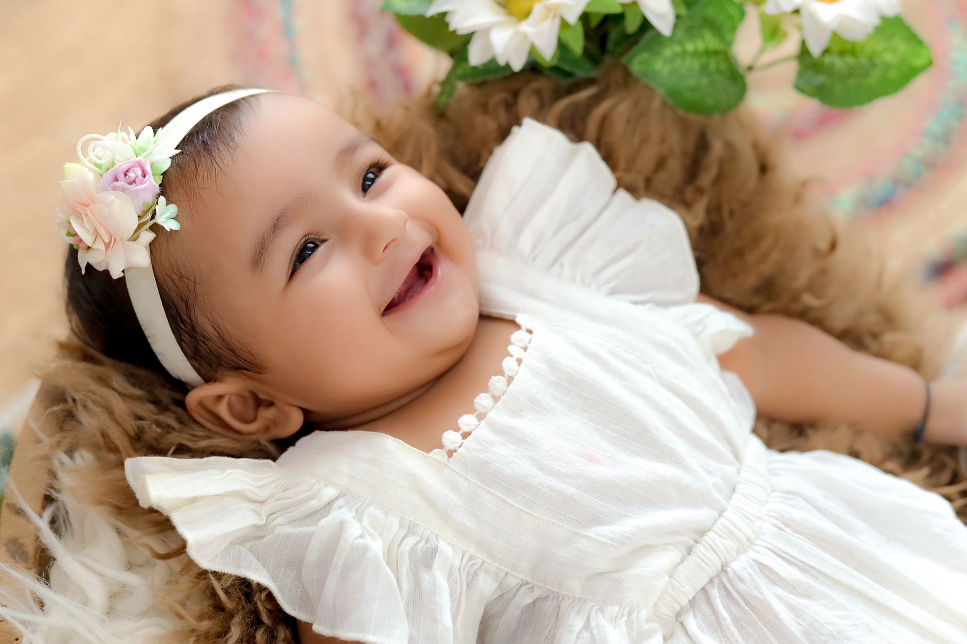 Ilustrasi: Charming baby wearing a floral headband, smiling in a white dress with delicate ruffles.