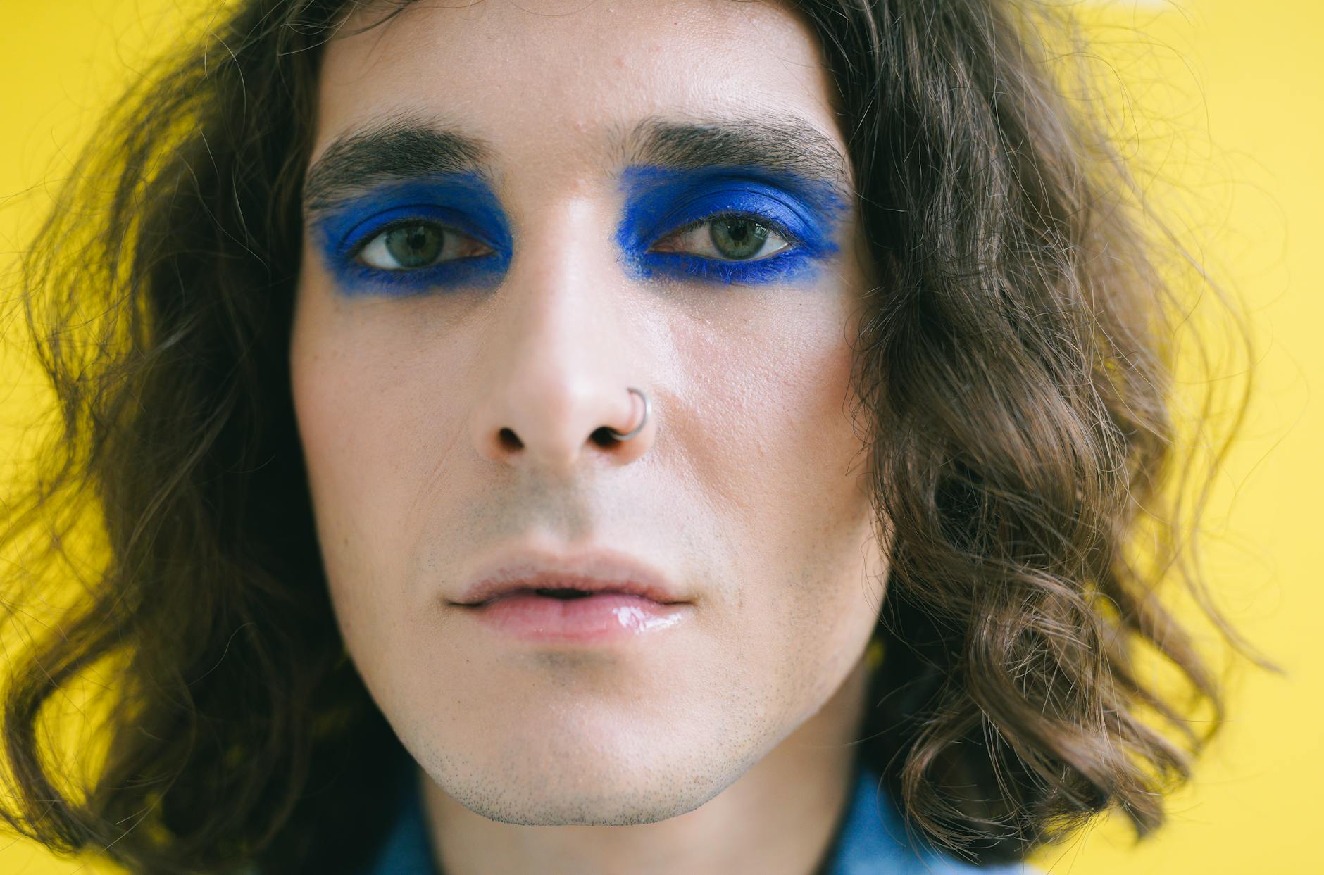 Ilustrasi: Close-up portrait of a person with striking blue eye makeup against a yellow backdrop.