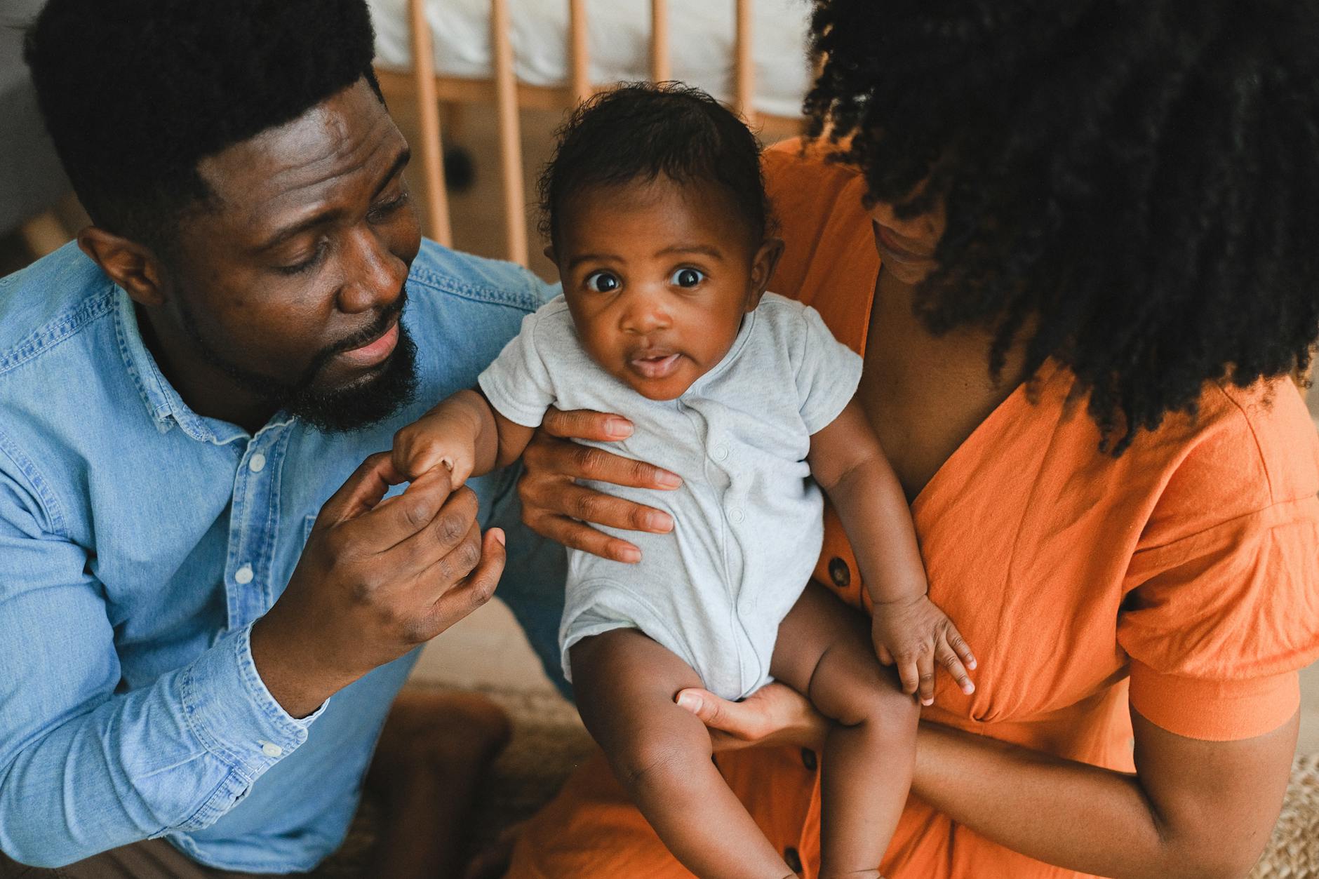 Ilustrasi: Loving parents holding adorable baby in a warm, intimate home environment.