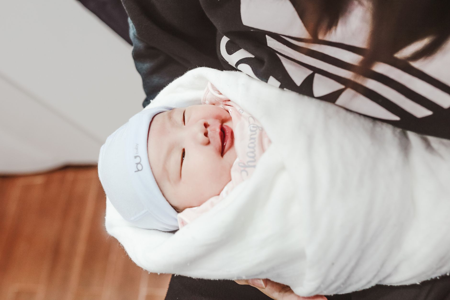 Ilustrasi: From above of adorable smiling newborn baby in light blue cap wrapped in soft white blanket lying on hands of mother