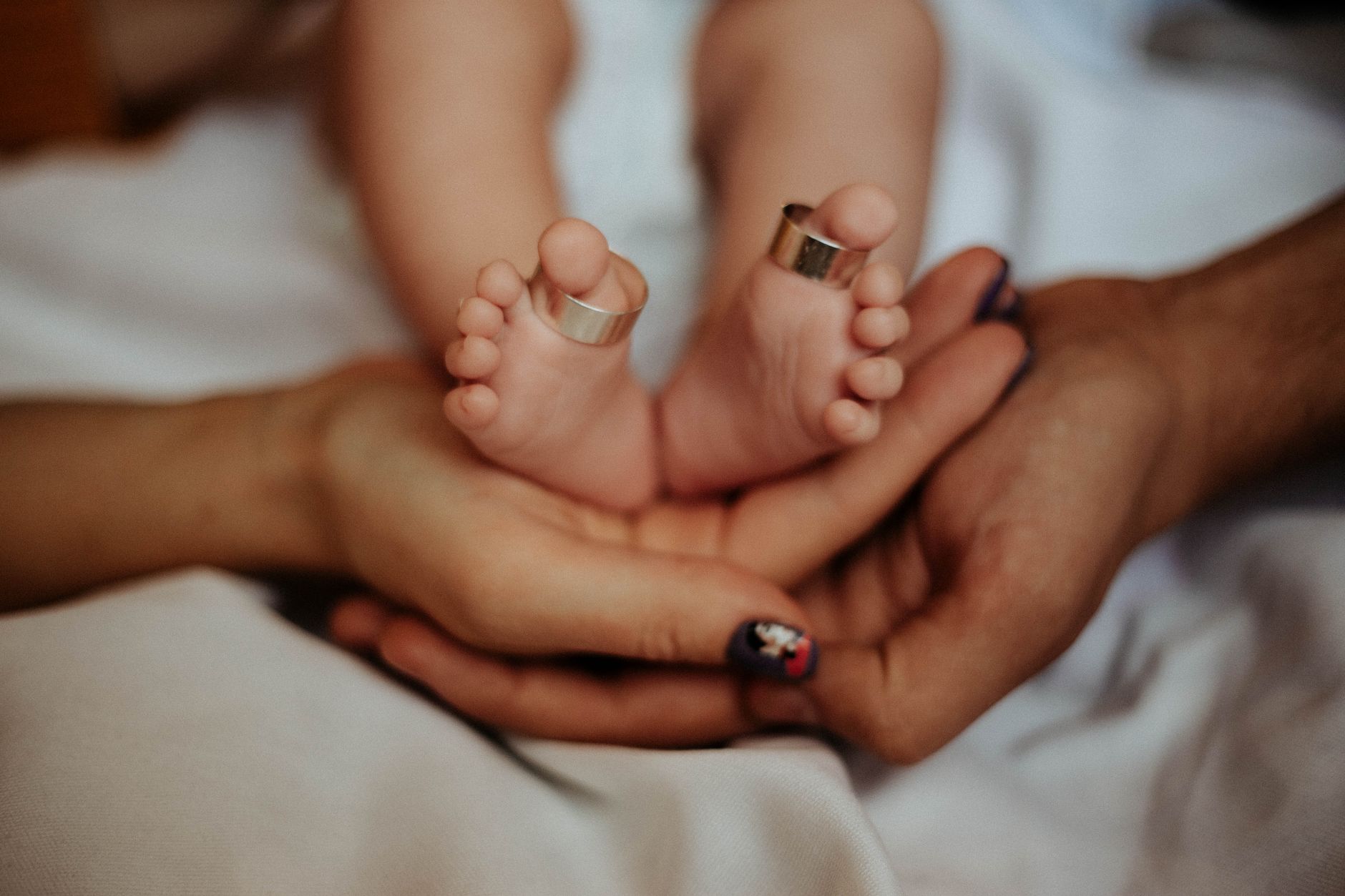 Ilustrasi: A close-up of baby feet with wedding rings nestled in parents' hands, symbolizing love and family.