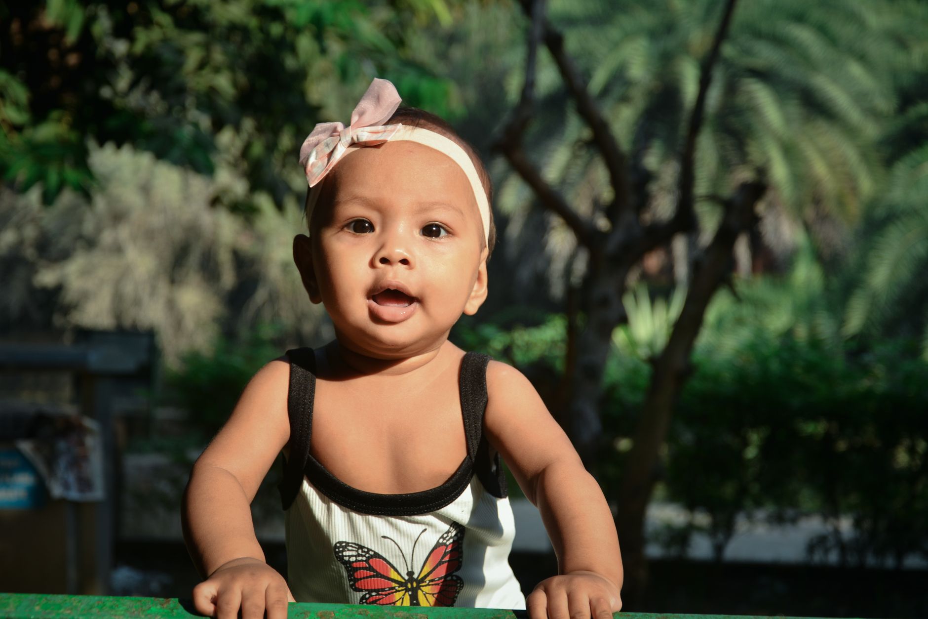 Ilustrasi: Cute baby girl with a butterfly dress smiling outdoors during summer.