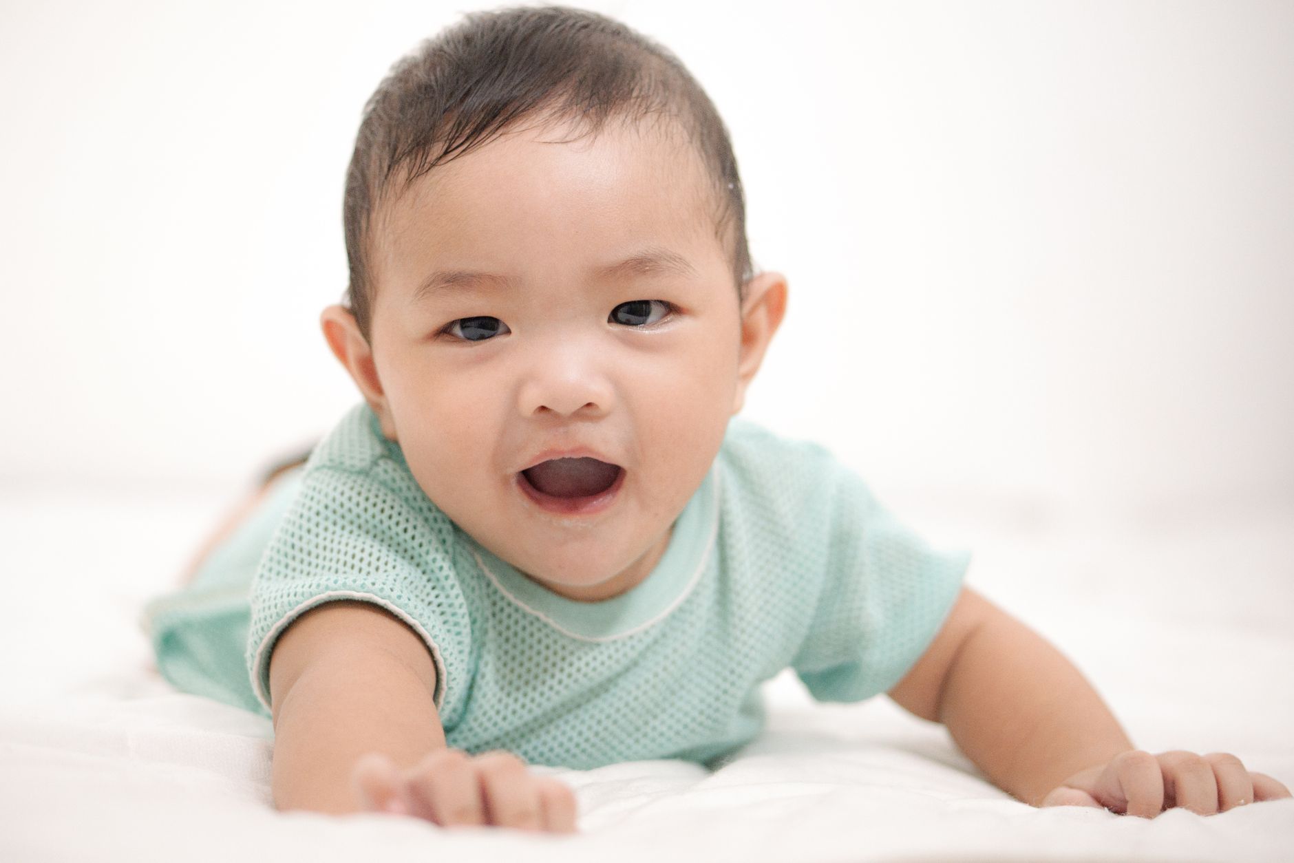 Ilustrasi: A cute Asian baby boy smiling while lying on a white background.