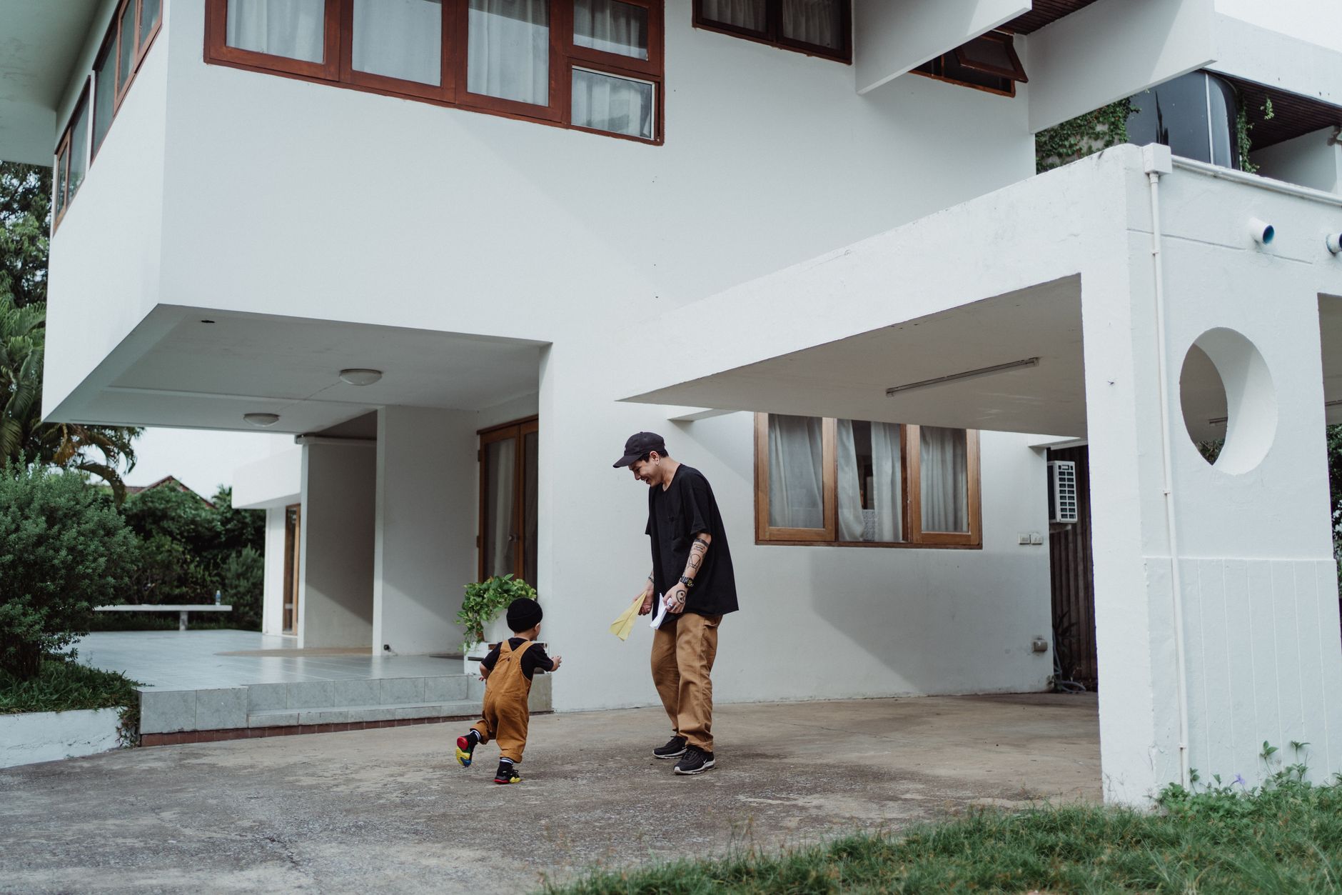 Ilustrasi: Father and son enjoying playful bonding time in front of a modern house.