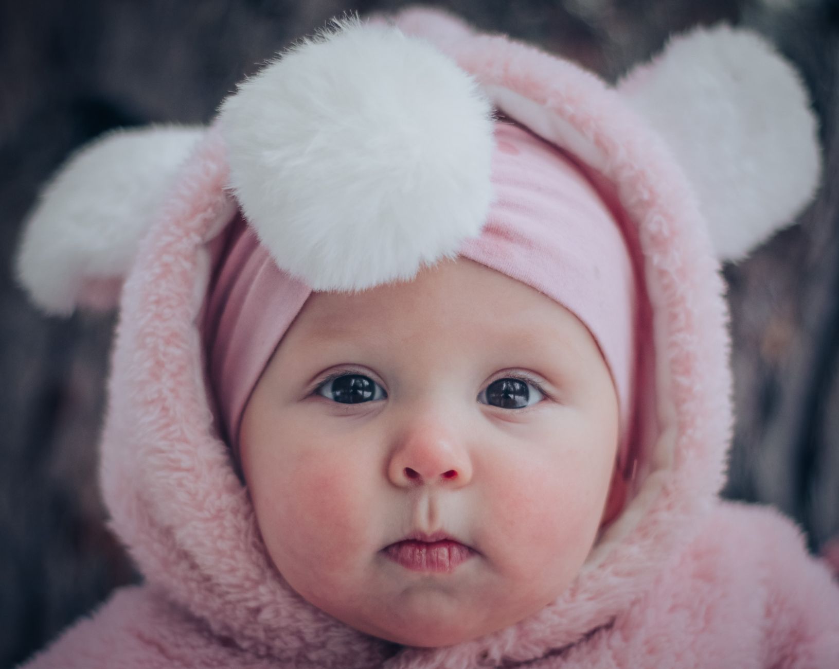 Ilustrasi: Cute baby in a pink fluffy hoodie with adorable pom pom ears. Close-up portrait.