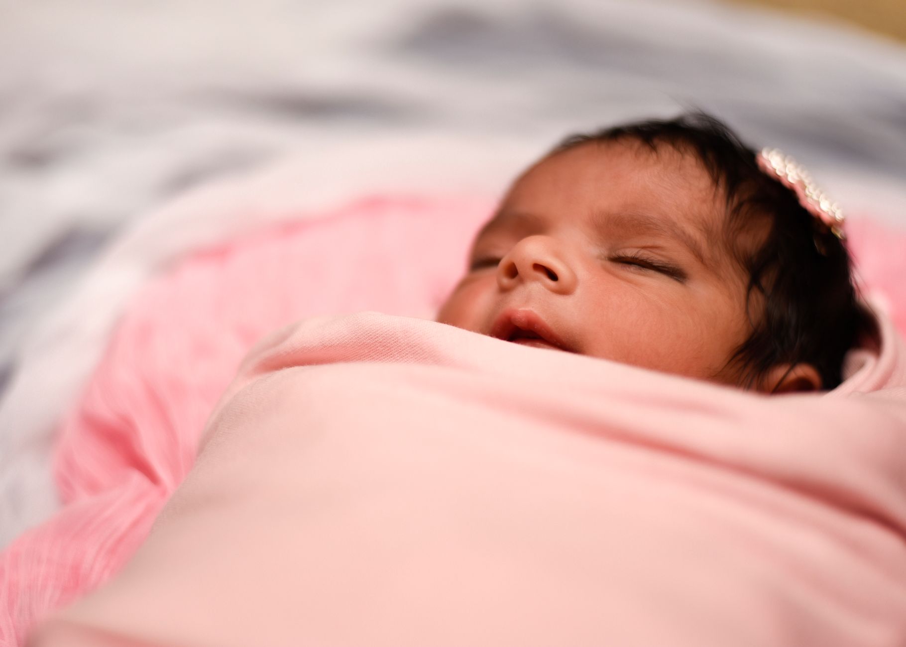 Ilustrasi: A serene image of a newborn baby wrapped in a soft pink blanket, peacefully sleeping.