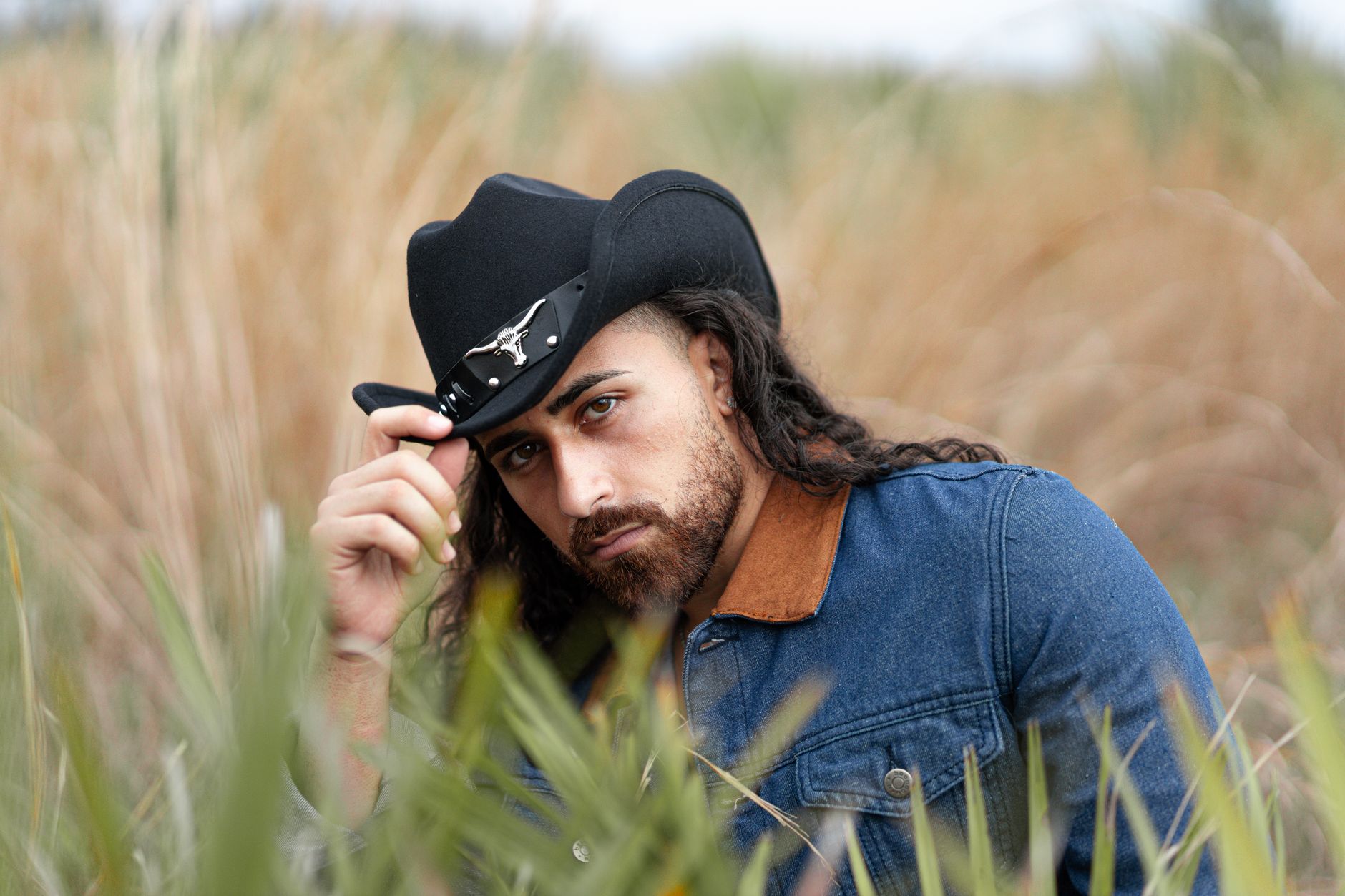 Ilustrasi: Portrait of a young man wearing a cowboy hat outdoors in a natural setting, embodying a Western style.