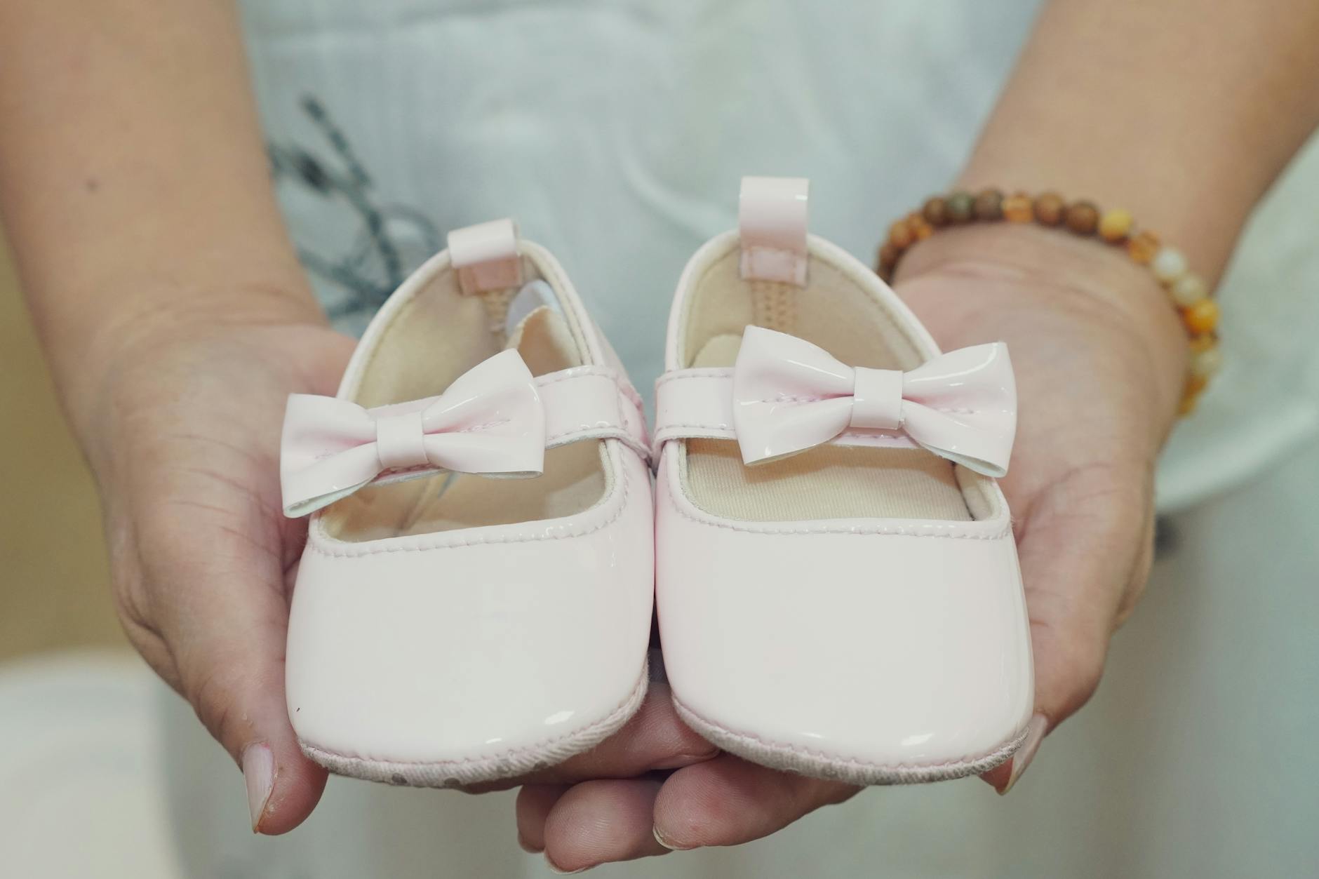 Ilustrasi: Adorable baby shoes with bows held in hands, perfect for a baby girl announcement or gift idea.