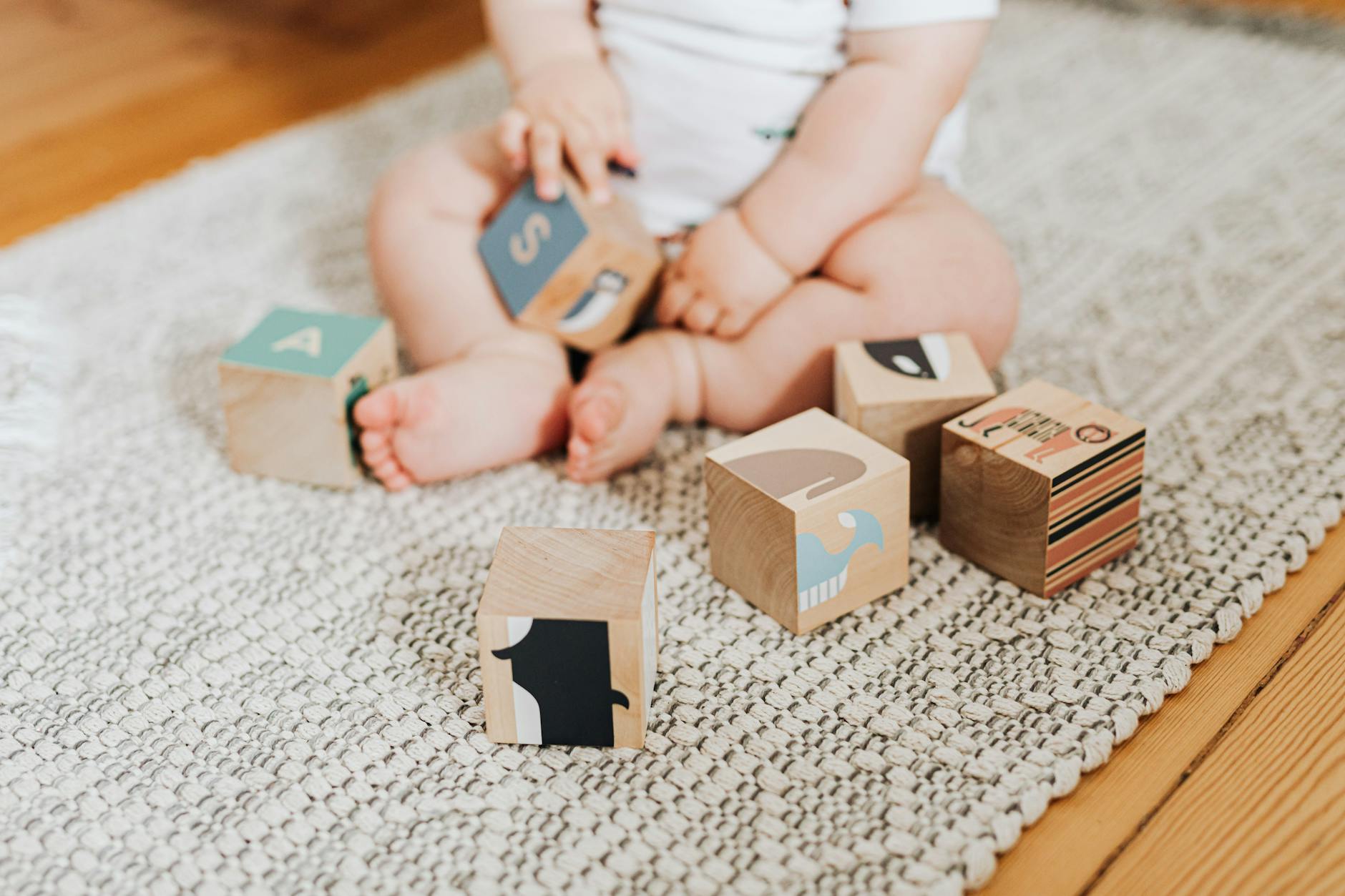 Ilustrasi: Adorable baby sitting on a rug and bermain with colorful wooden blocks.